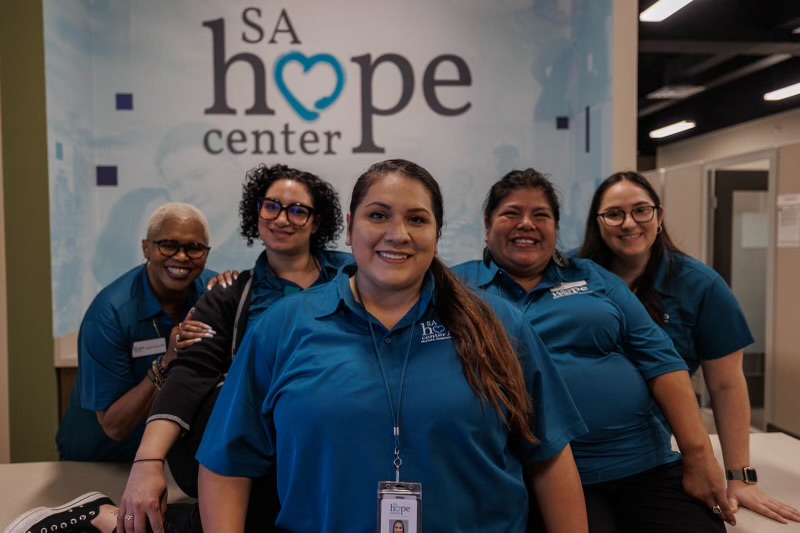Group of five women in blue shirts smiling in front of a Hope Center sign.