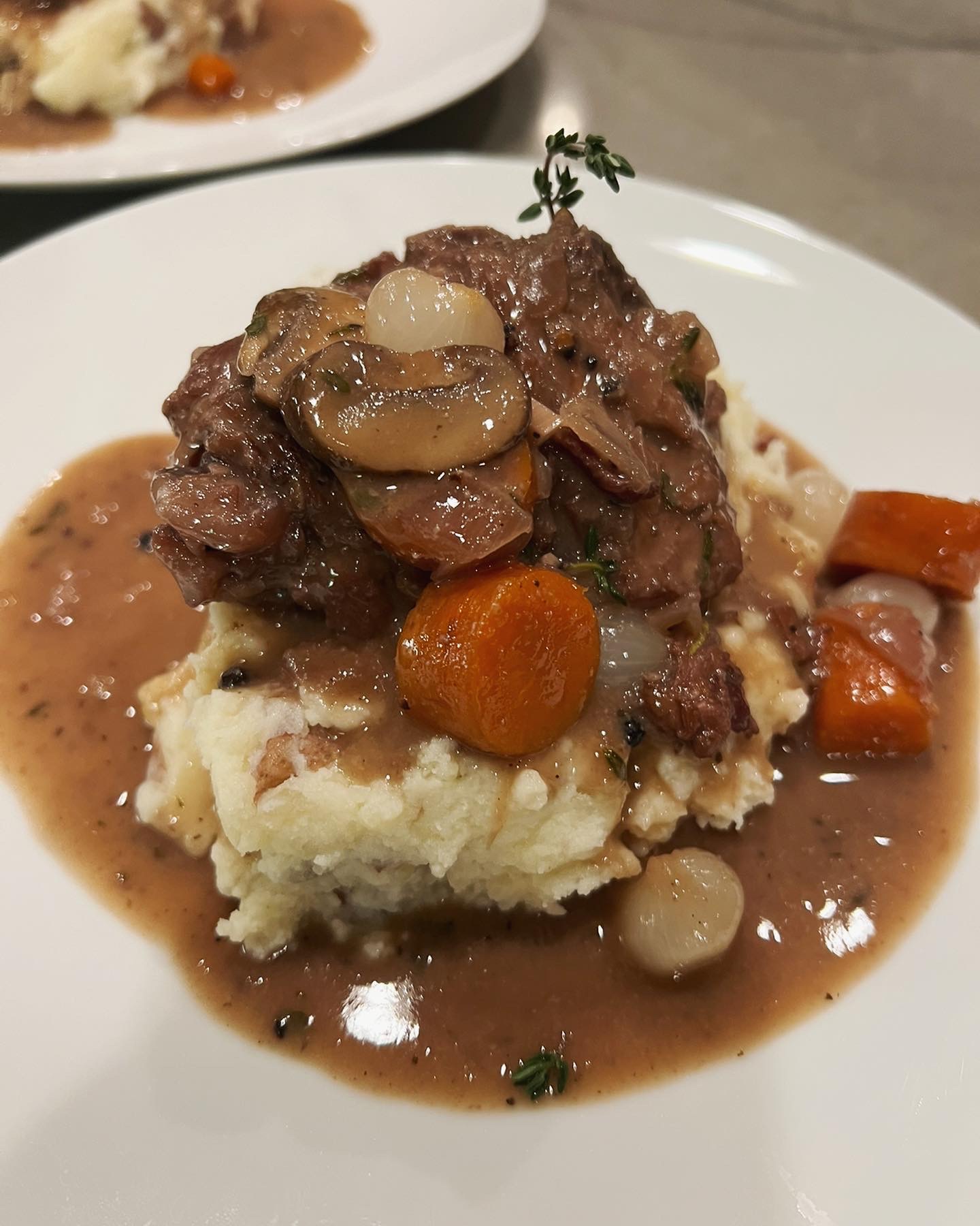 Stew with meat, mushrooms, and vegetables served over mashed potatoes on a white plate.