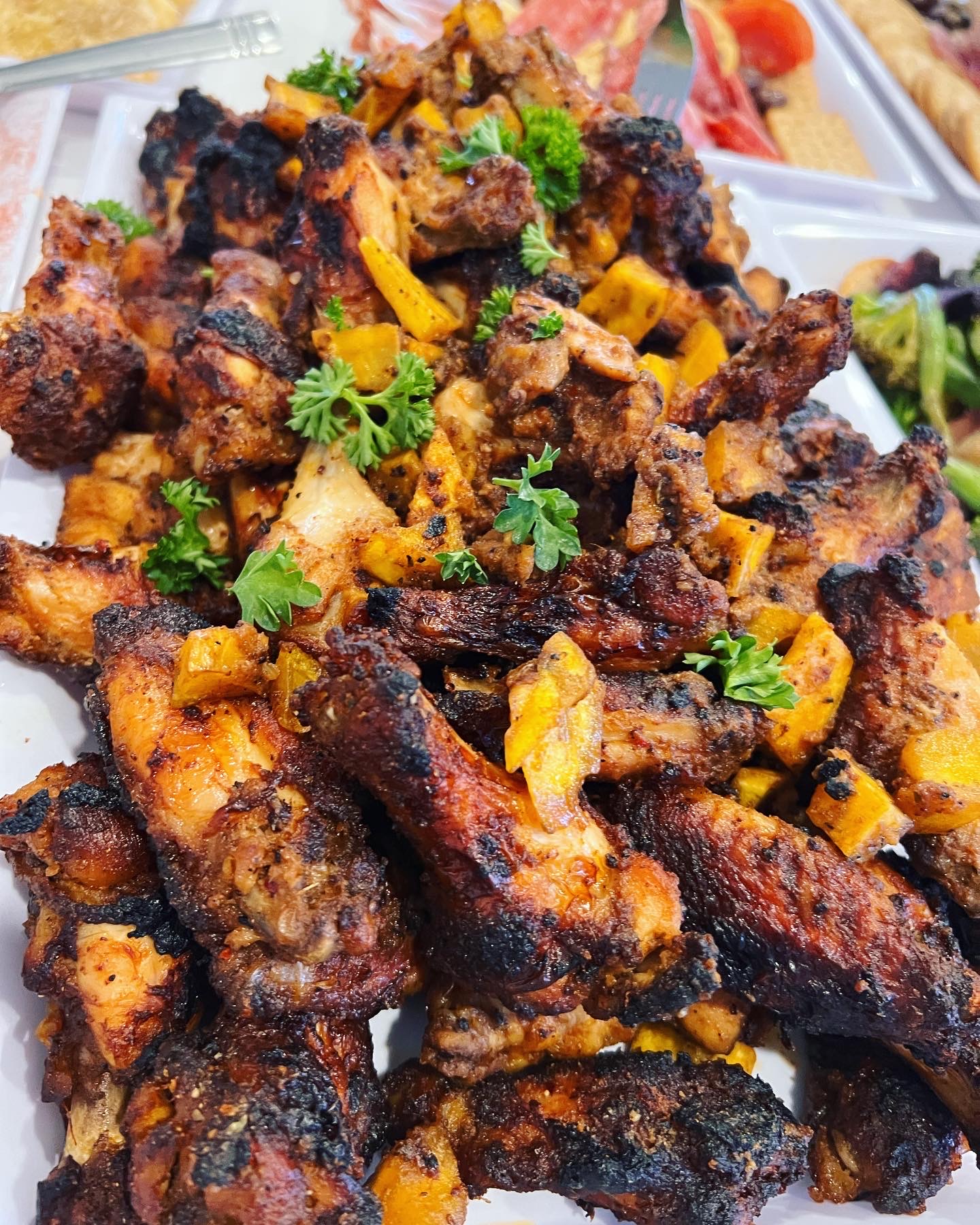 Plate of grilled chicken pieces garnished with cilantro and yellow spices, with other food items in the background.