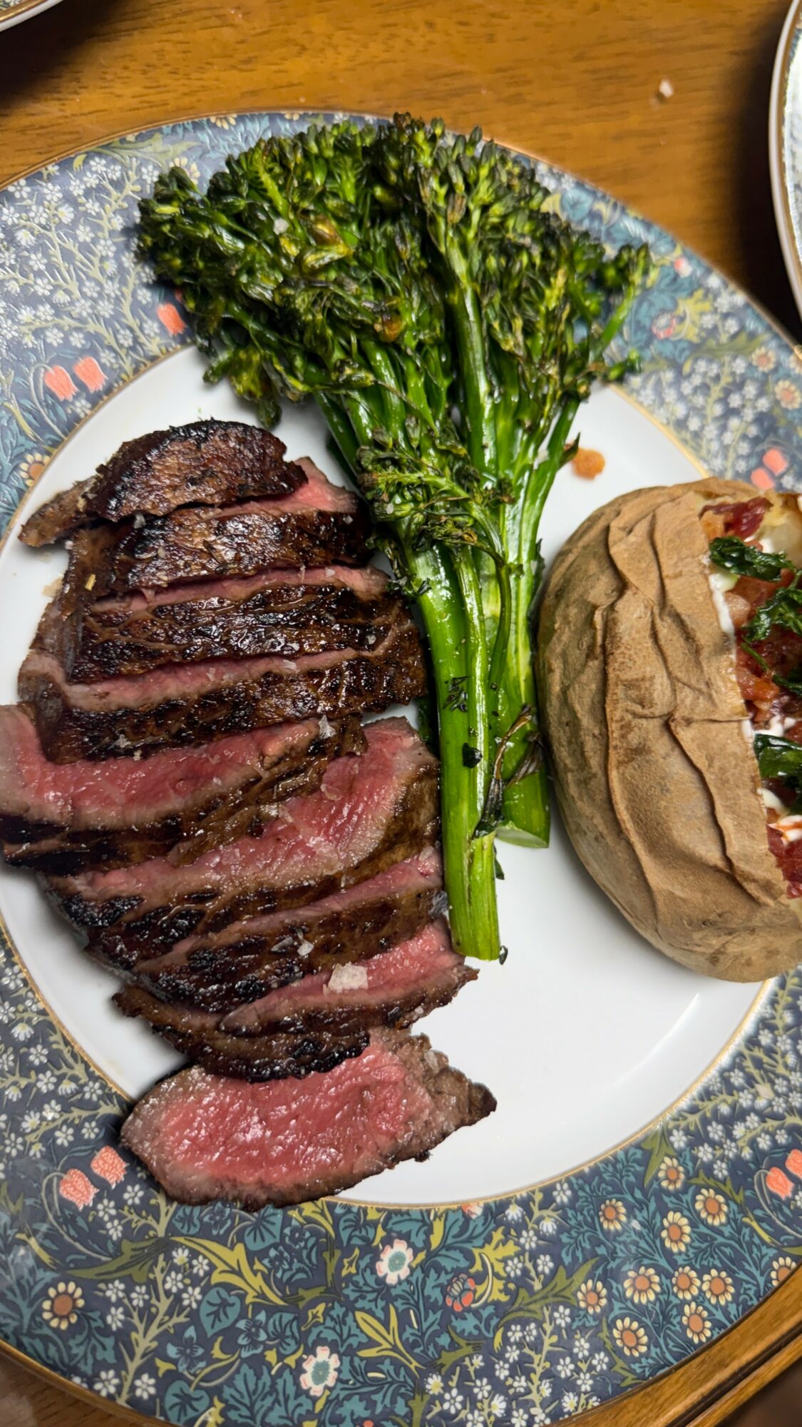 Sliced cooked steak, grilled broccoli, and a stuffed pita on a decorative plate.