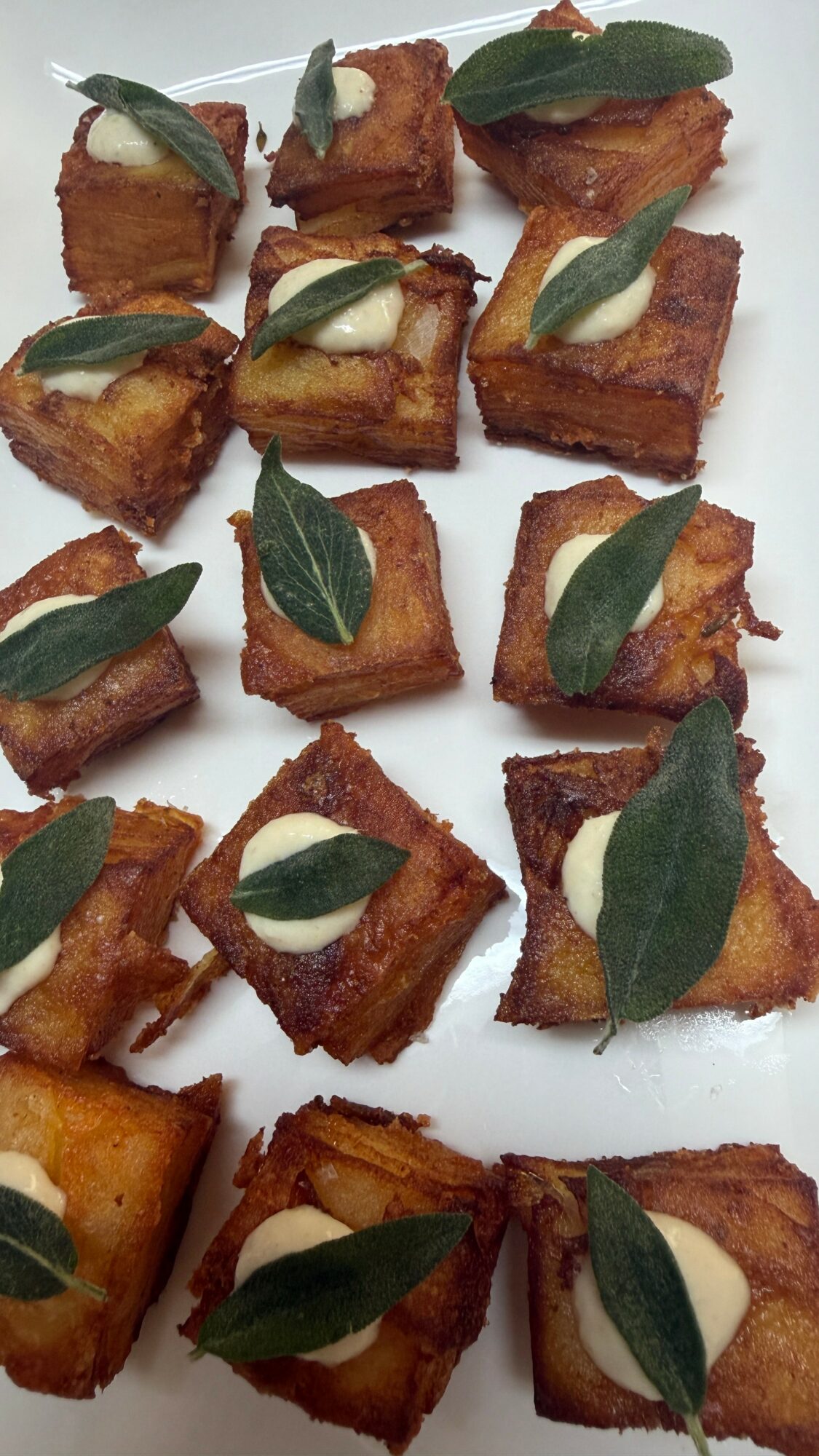 Small fried food pieces garnished with green leaves arranged on a white plate.
