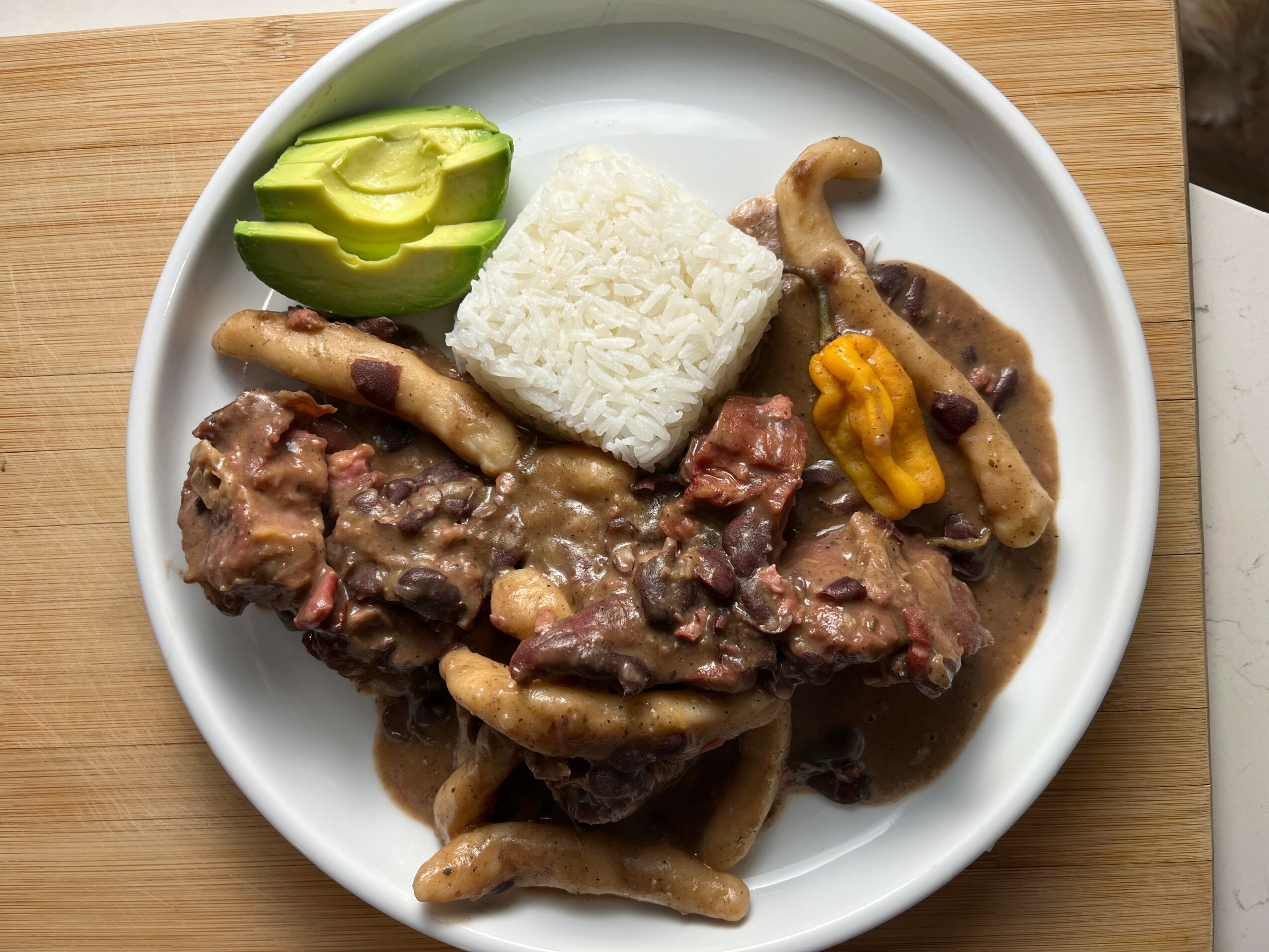 Plate with rice, sliced avocado, and cooked meat with mushrooms and sauce.