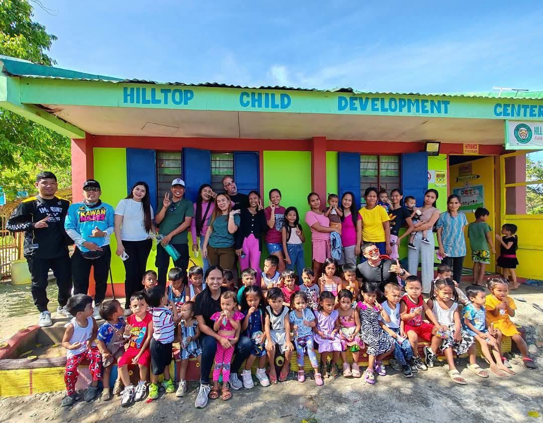 Group of children and adults standing outside a colorful building with a sign reading Hilltop Child Development Center.