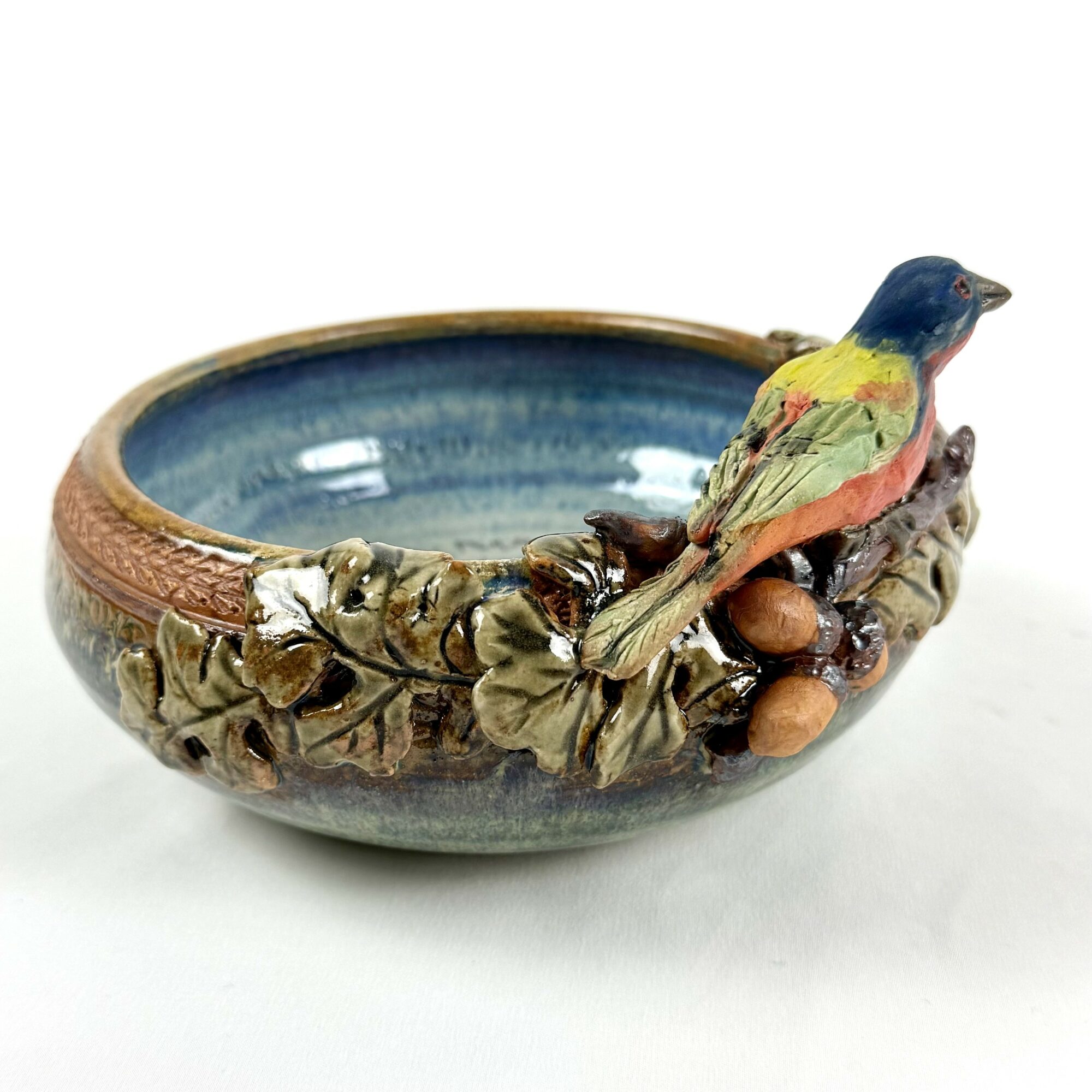 Decorative ceramic bowl with a colorful bird and foliage design on the side, glazed in blue and earthy tones.