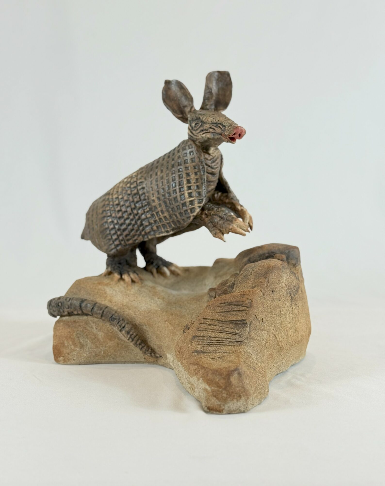 A sculpture of a mouse with textured body, standing on a wooden log, with a plain light background.