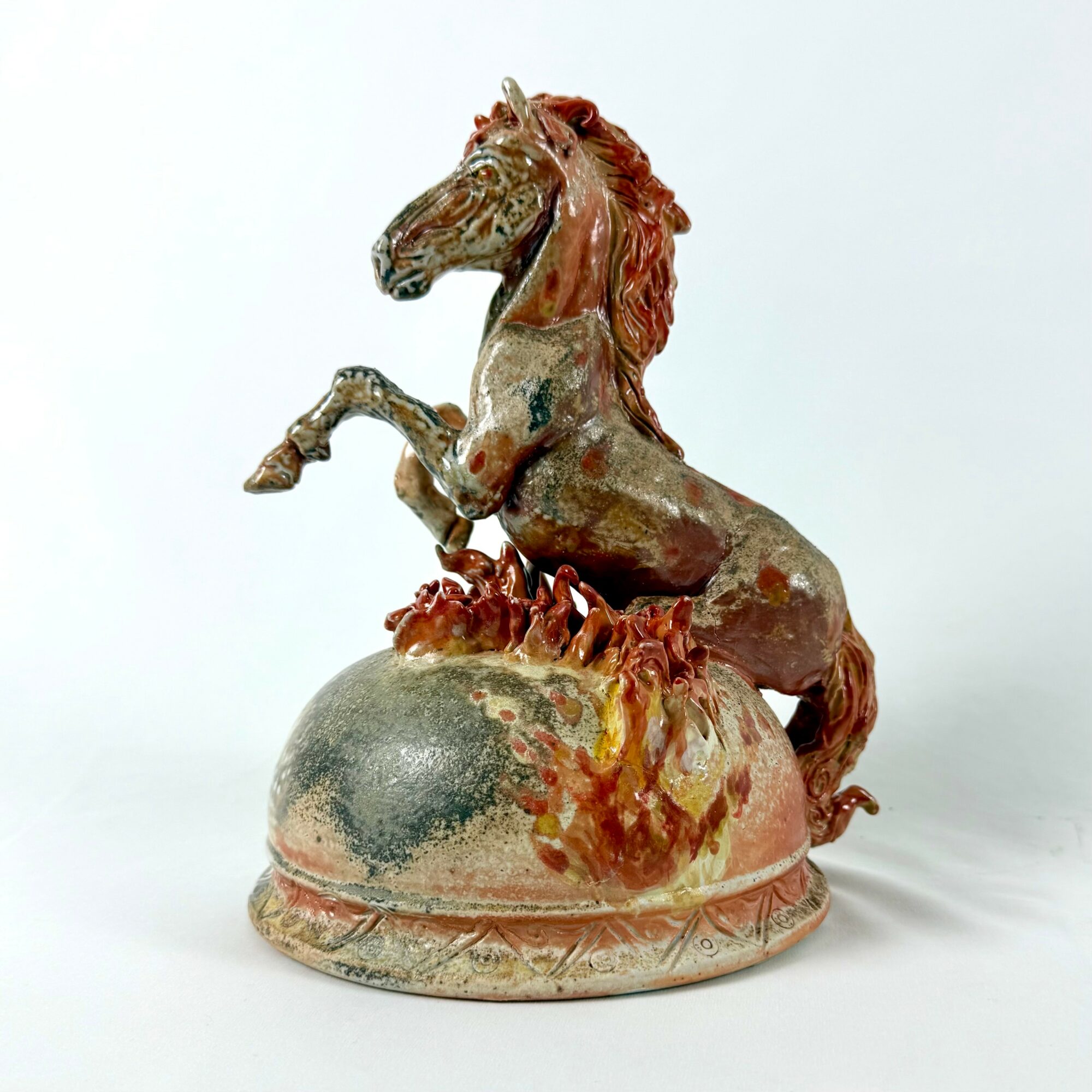Sculpture of a rearing horse on a decorated base with flames, made of ceramic or similar material.