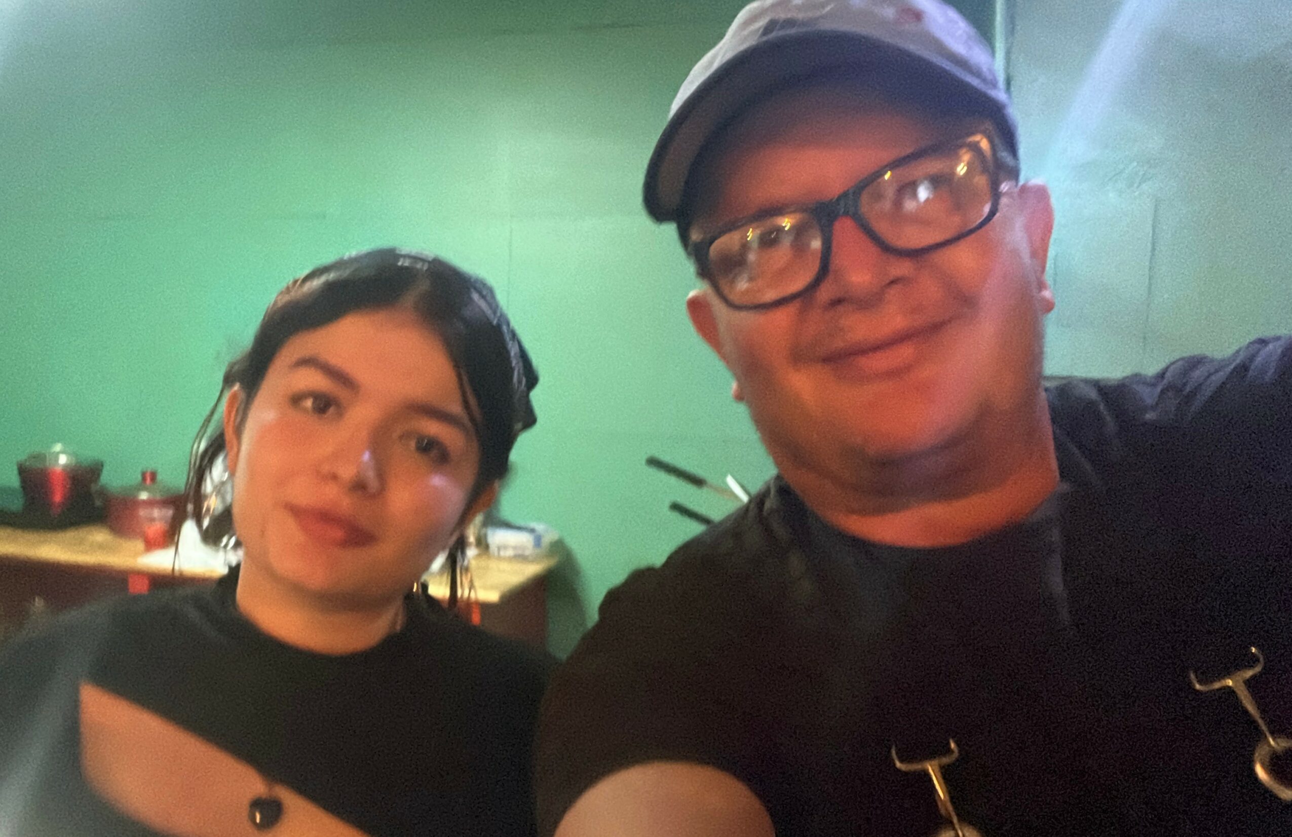 Two people taking a selfie indoors with a green wall in the background.