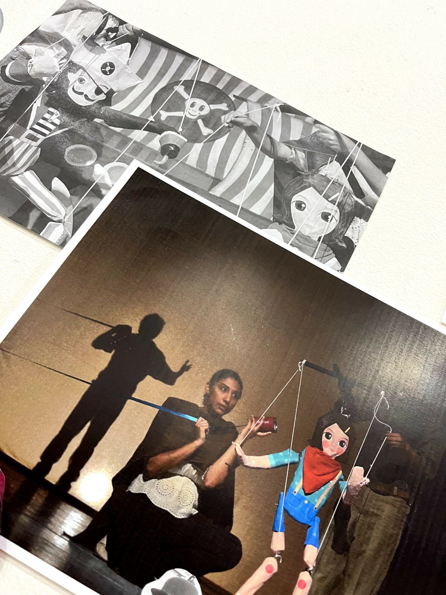 Person performing puppet show with puppet character, shadow cast on wall, puppet dressed in blue and red, holding strings.