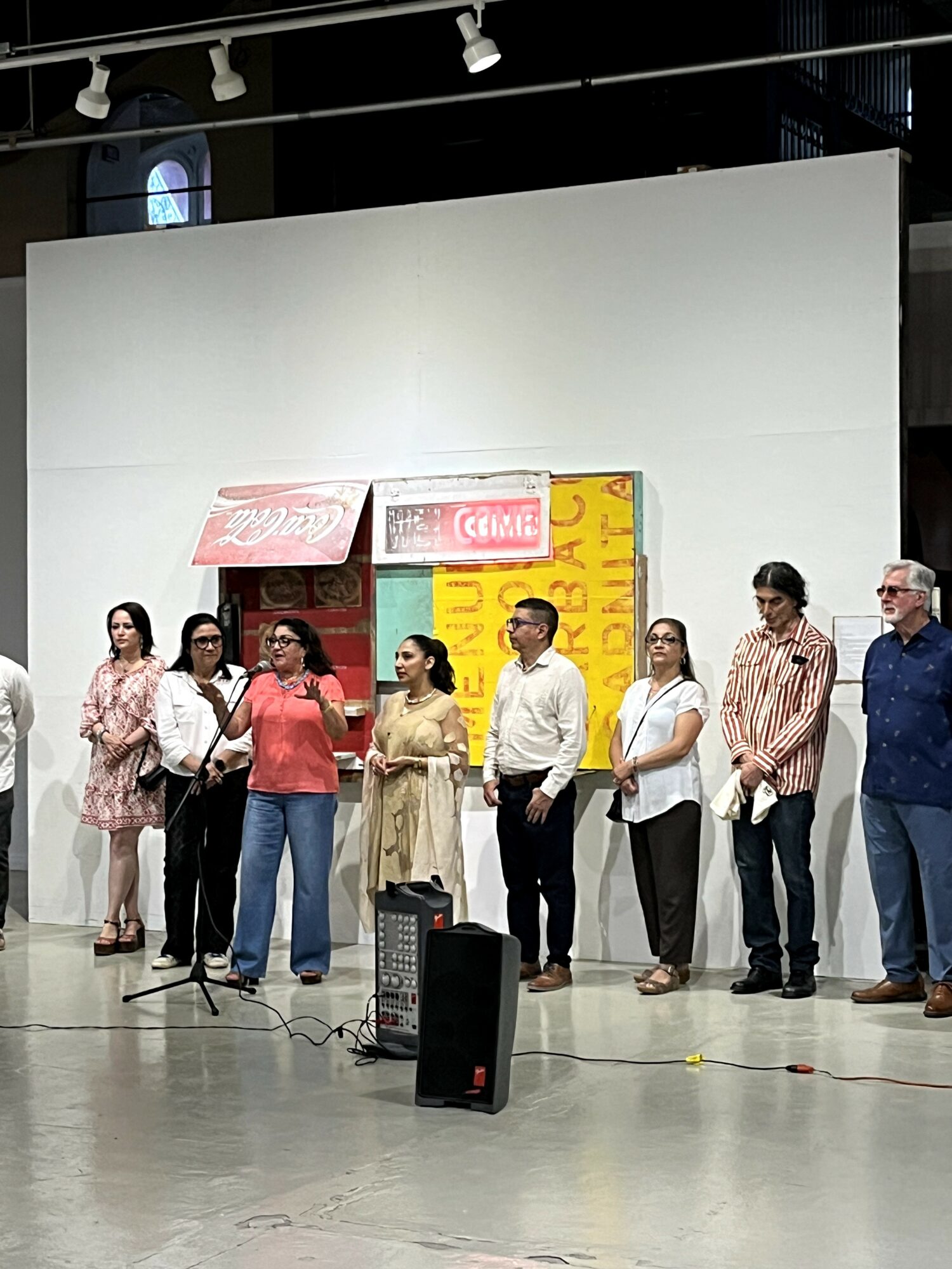 Group of eight people standing in a line on stage, with a white backdrop and colorful signs above them.