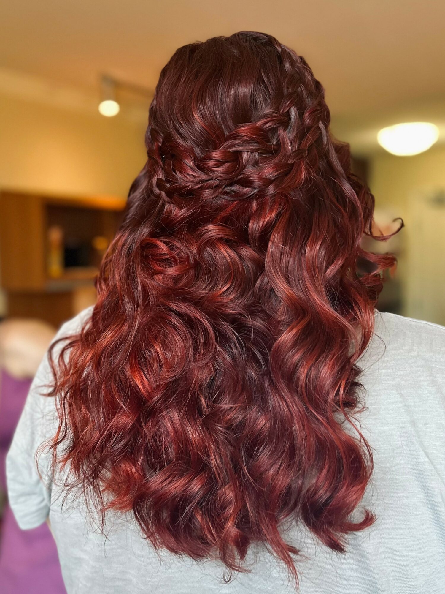 Person with long, wavy, reddish-brown hair styled in a braid on top, flowing down their back, indoors.