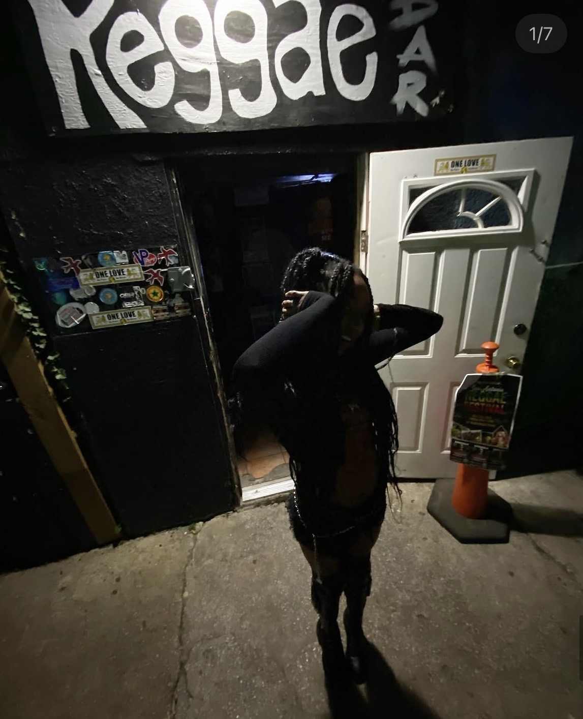 Person standing outside a door with a fire extinguisher nearby, nighttime scene, graffiti on wall, concrete ground.