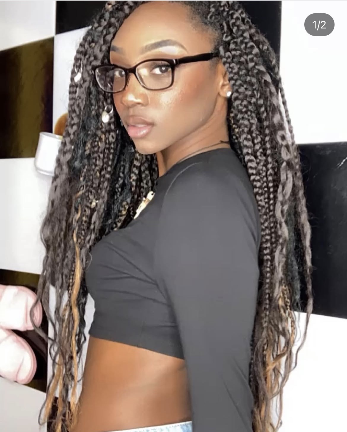 Woman with glasses and long braided hair, wearing a black crop top, looking over shoulder.