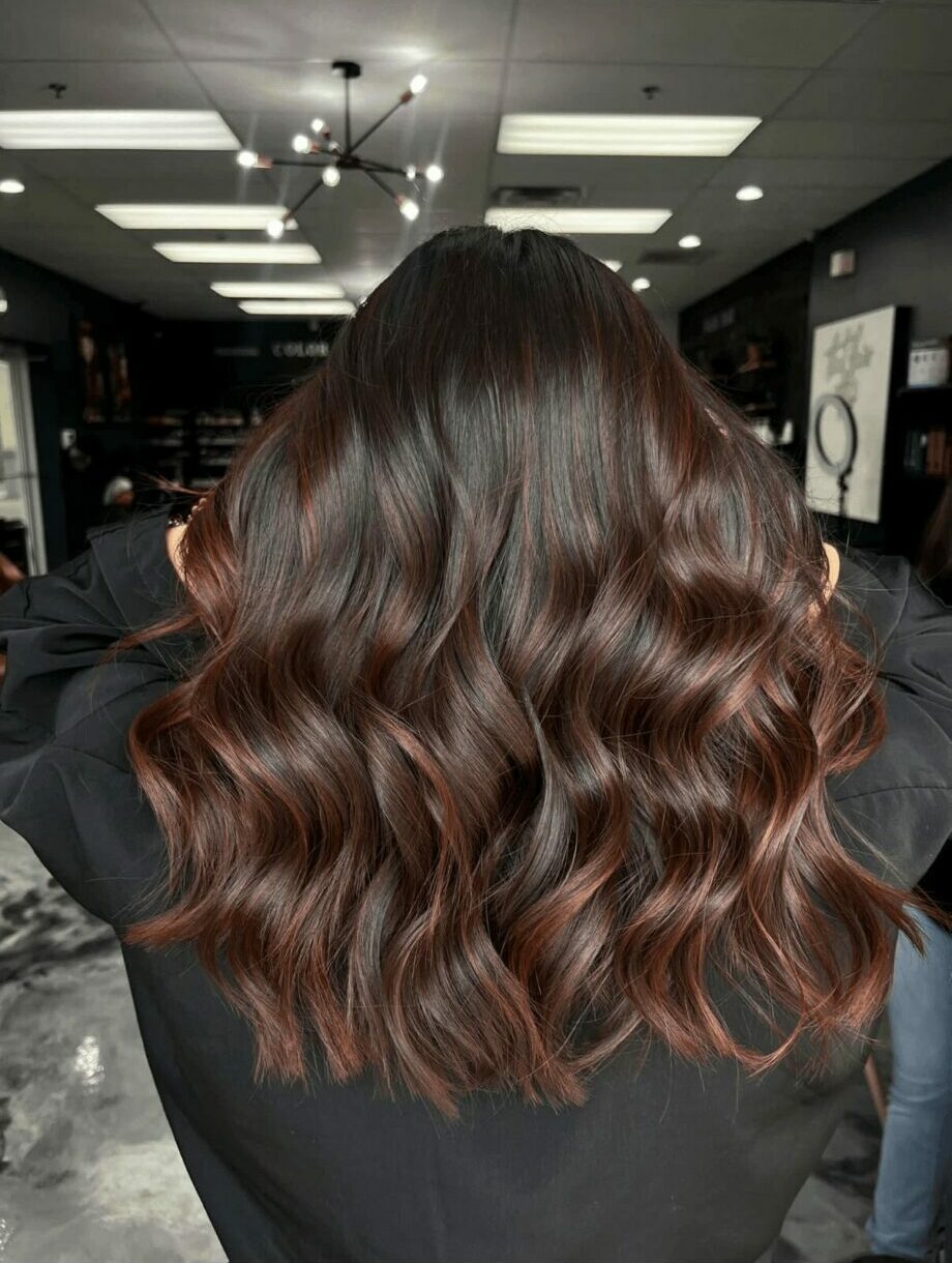 Back of a person with wavy, shoulder-length brown hair in an indoor setting.