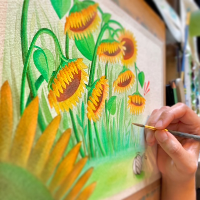 Person painting sunflowers with a small brush on a canvas, vibrant green and yellow colors, outdoor scene, hand visible