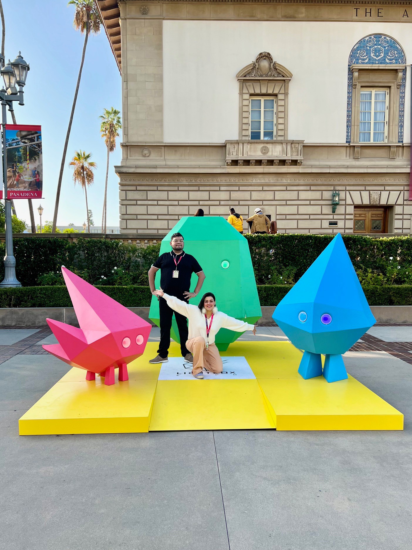 Three colorful cartoon-like sculptures of animals on a yellow platform outdoors, with a building and palm trees in background.