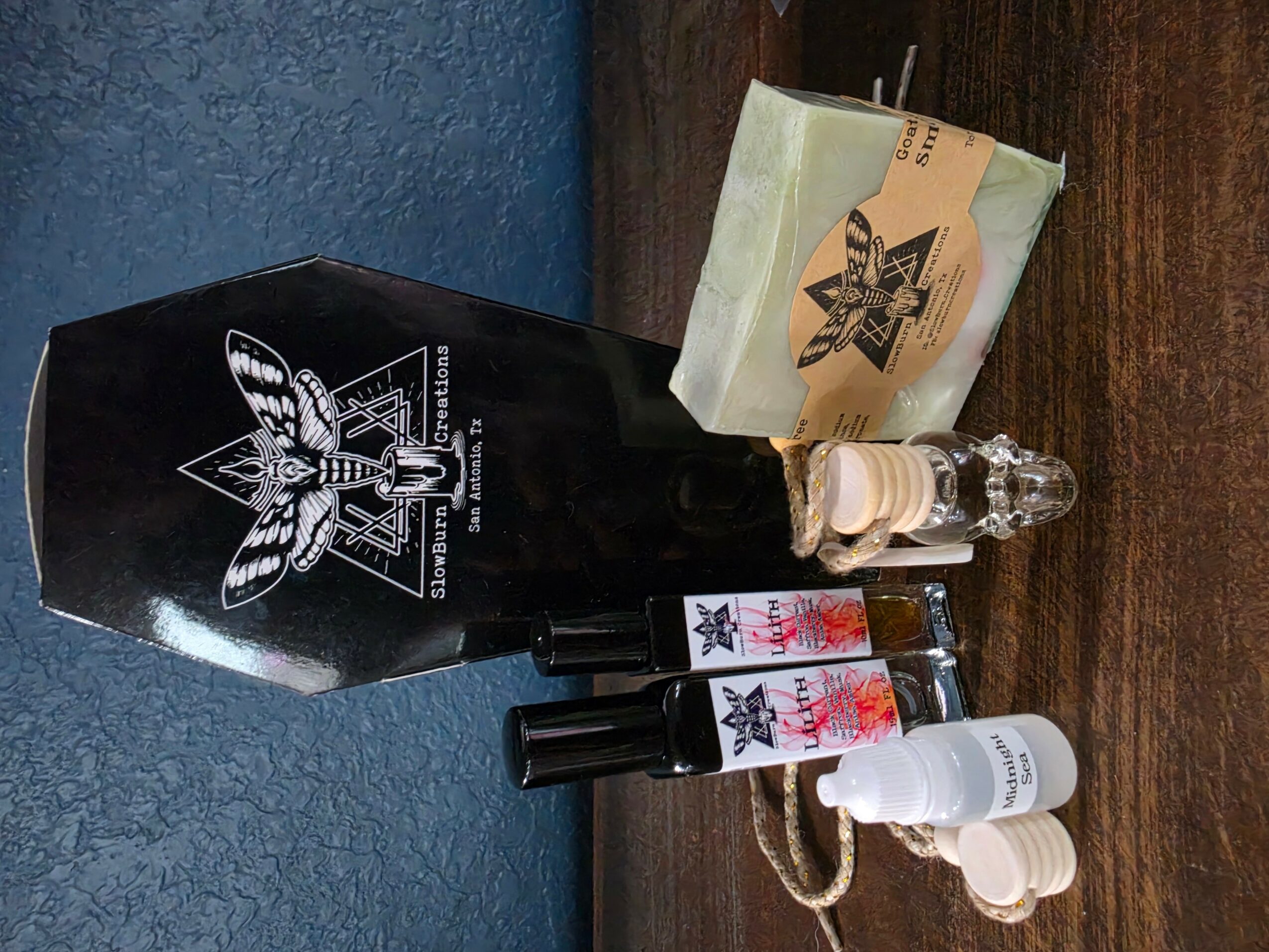 Black bottle with a bee logo, small bottles, and a white container on a wooden surface.