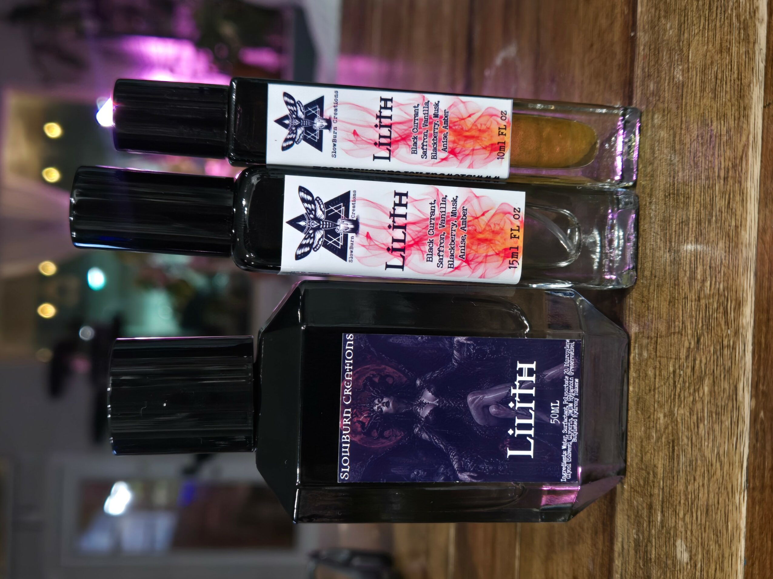 Three bottles and a box on a wooden surface, with colorful lights in the background.