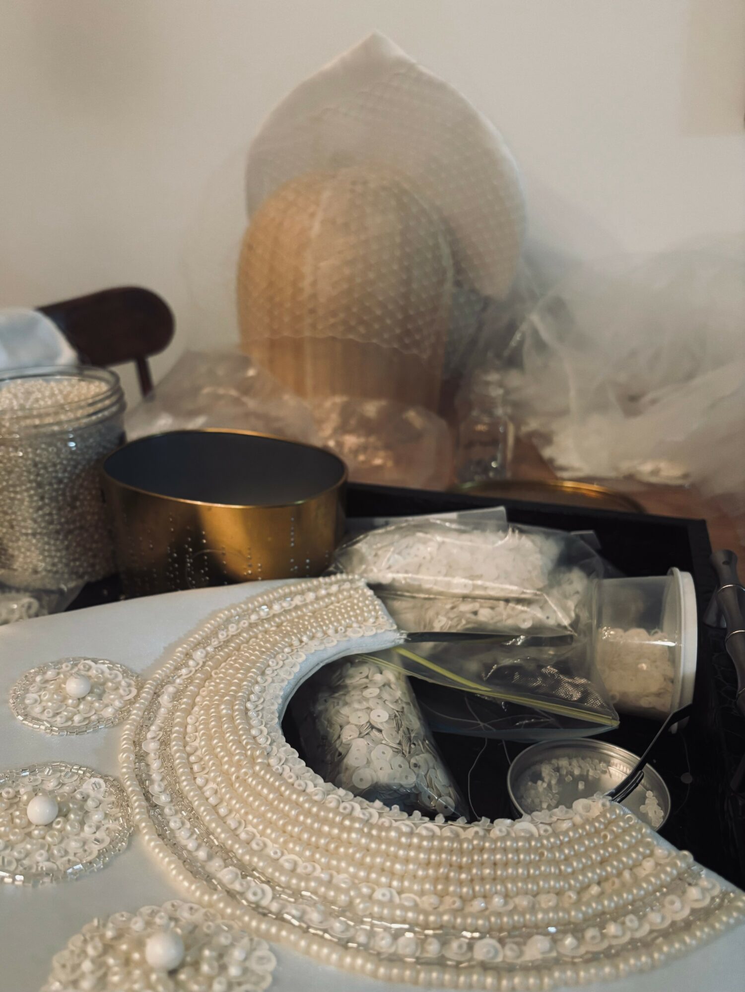 Decorative items including pearl necklaces, beads, and fabric, with a hat and other accessories in the background.
