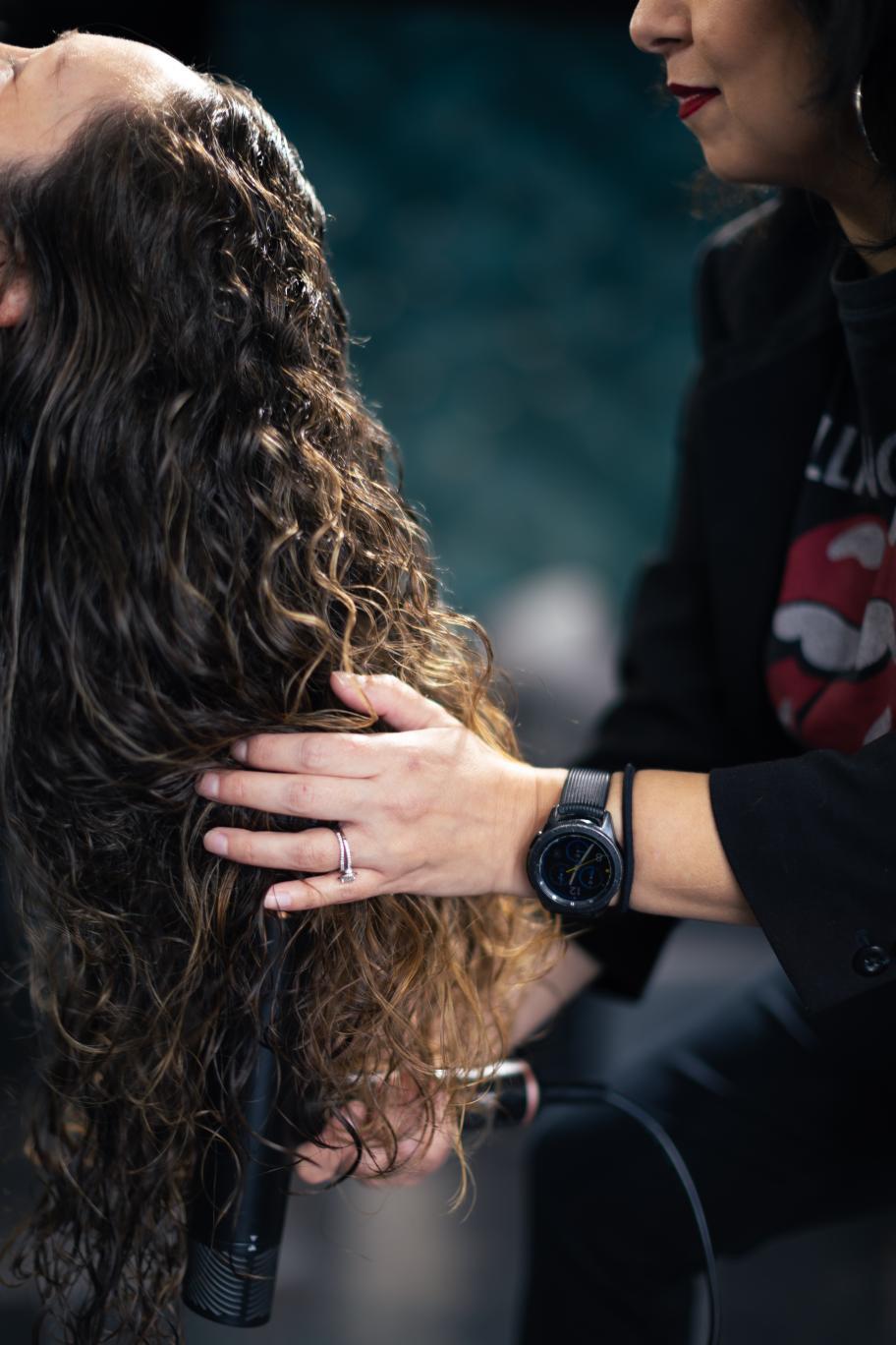 Person with curly hair being comforted by another person wearing a black shirt and watch, holding their shoulder.
