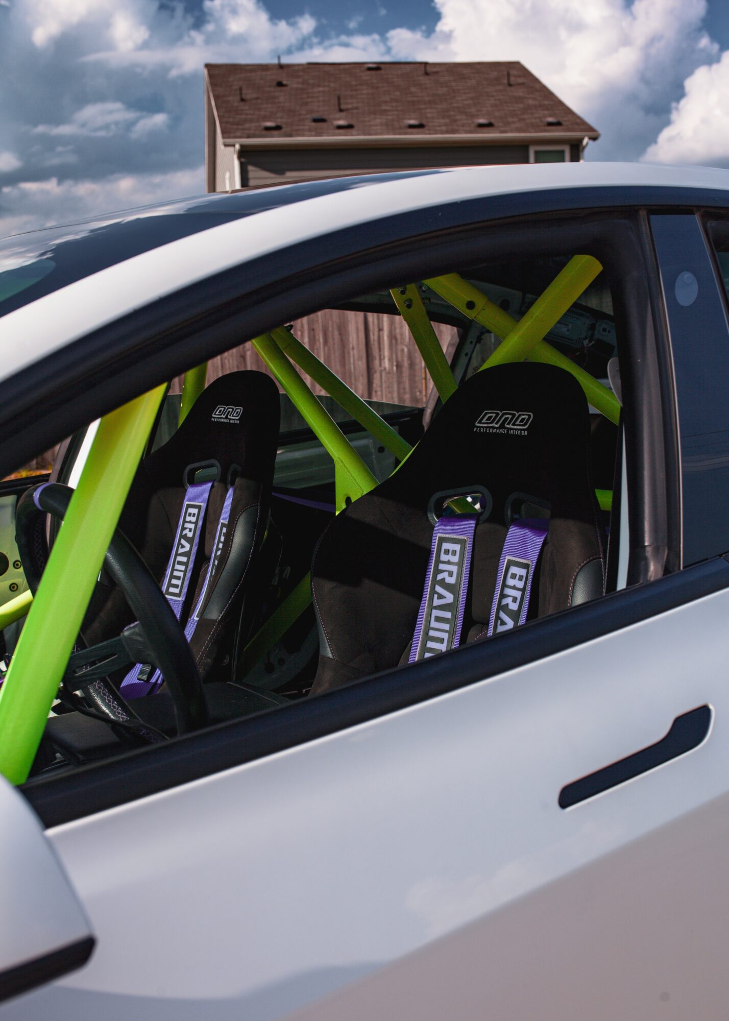View of a car interior with racing seats and a green roll cage, seen through the open window.
