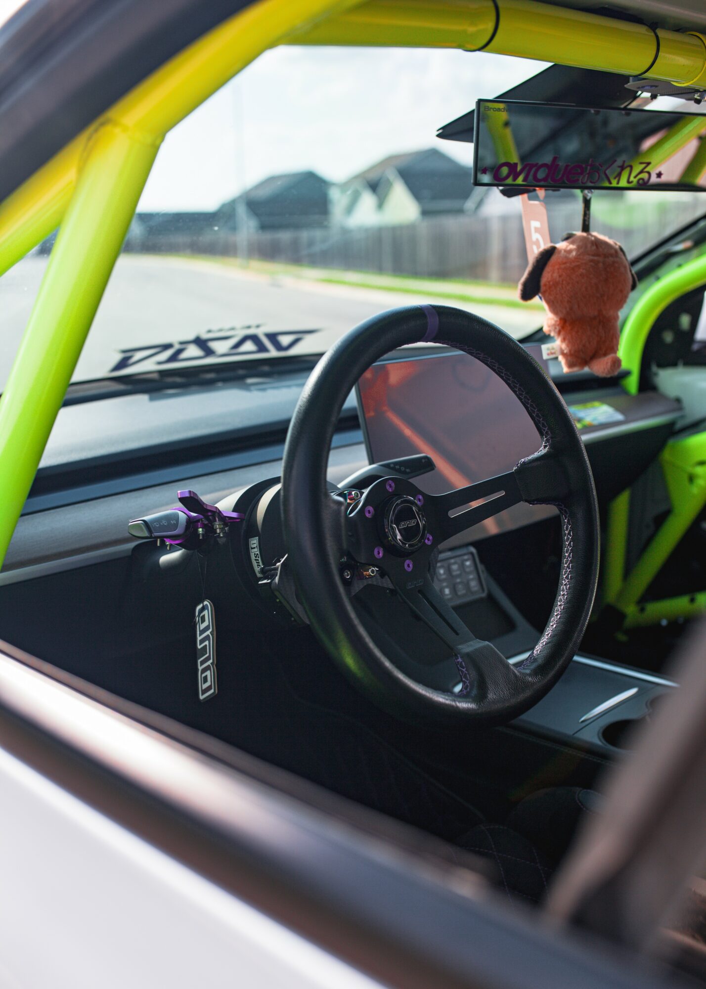 View of a car interior showing a steering wheel, dashboard, and a plush toy hanging from the rearview mirror.