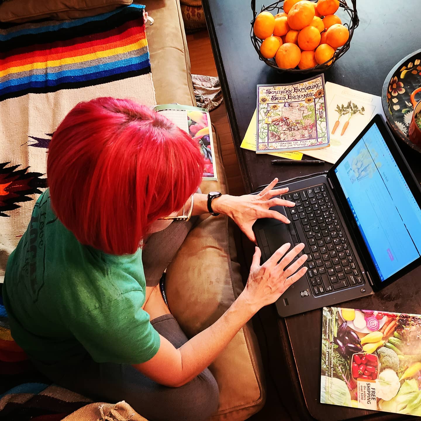 Woman with red hair working on a laptop at a table with oranges and colorful books.