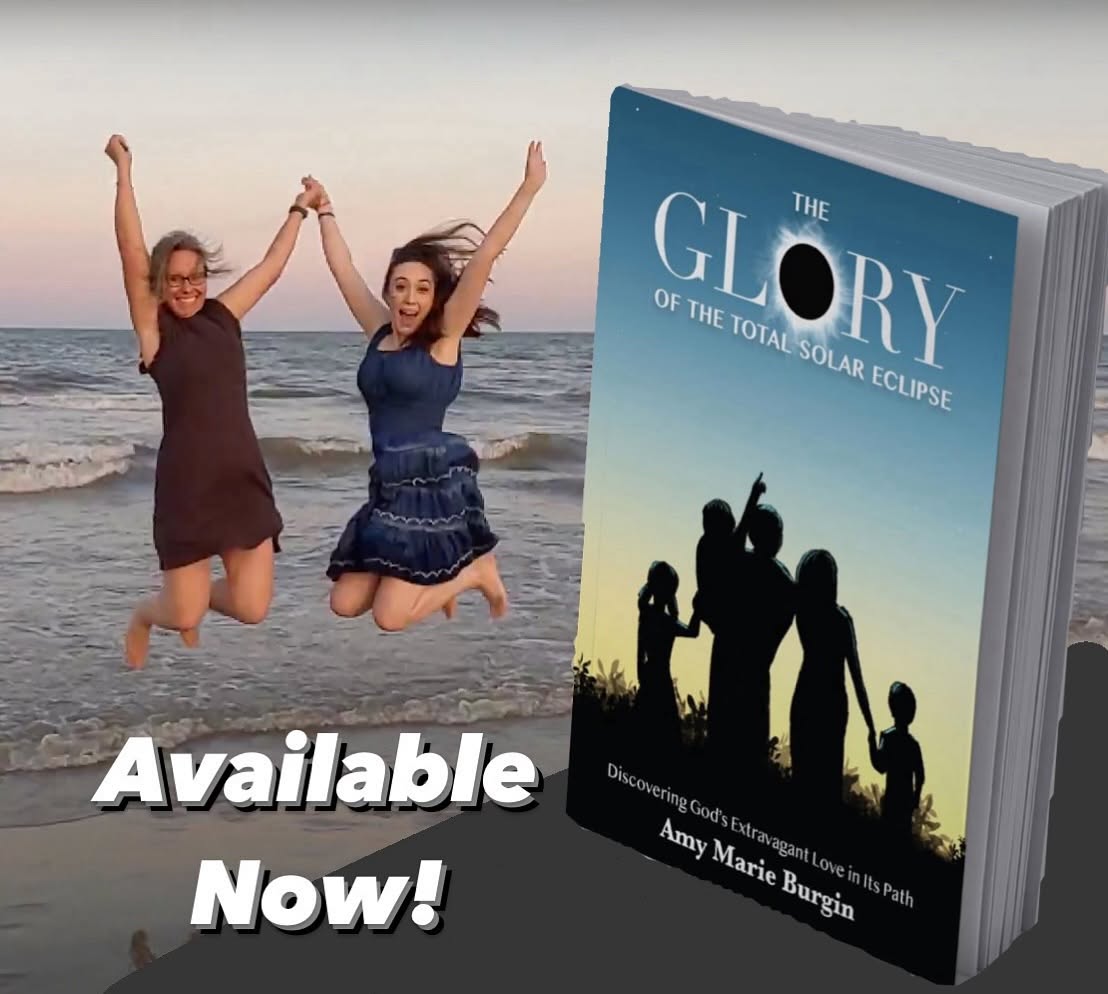 Two women jumping on the beach holding hands, with a book titled 'The Glory of the Total Solar Eclipse' by Amy Marie Burgin in the foreground. Text says 'Available Now!'.
