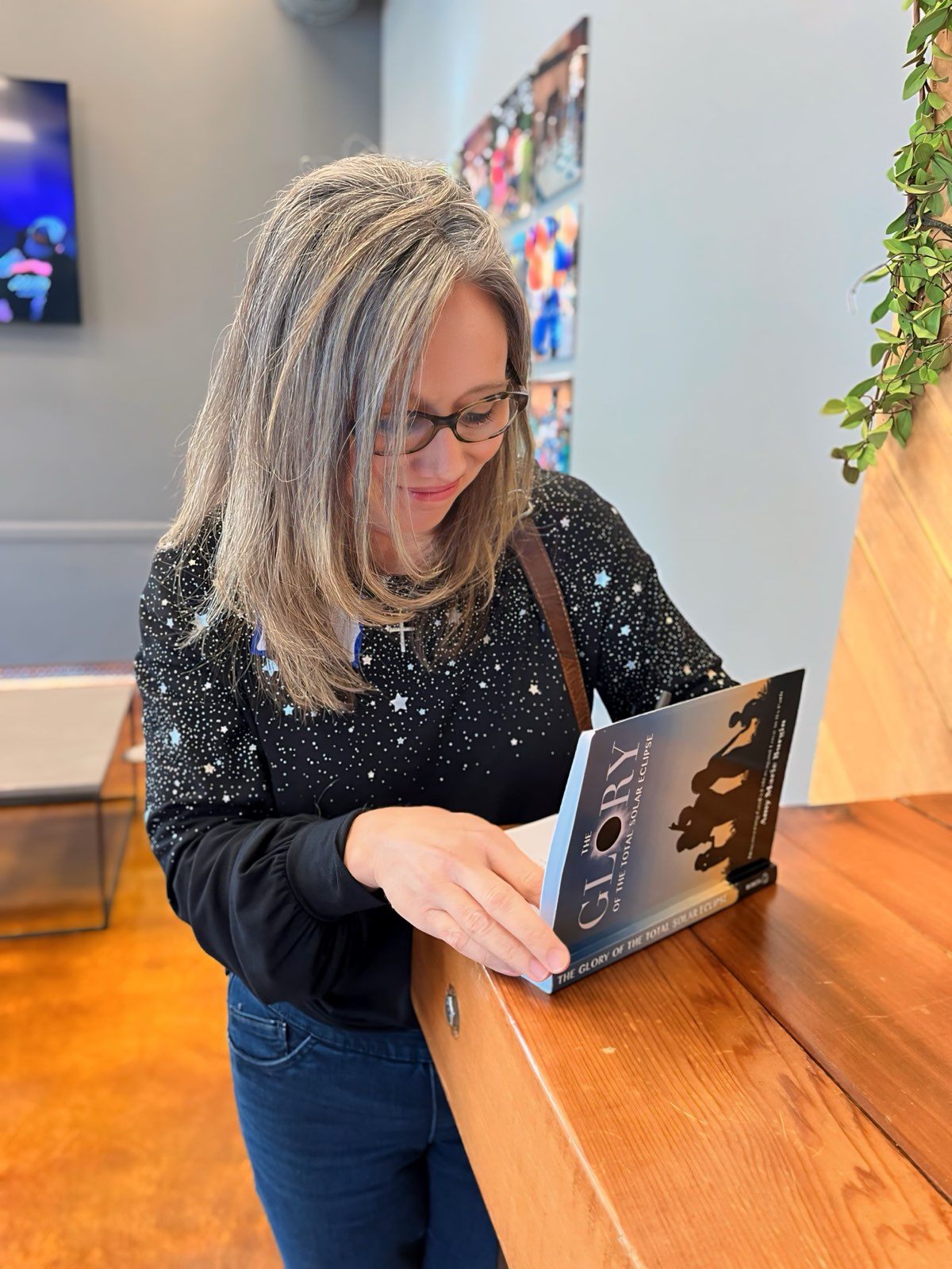 Woman with glasses and shoulder-length gray hair reading a menu at a wooden table.