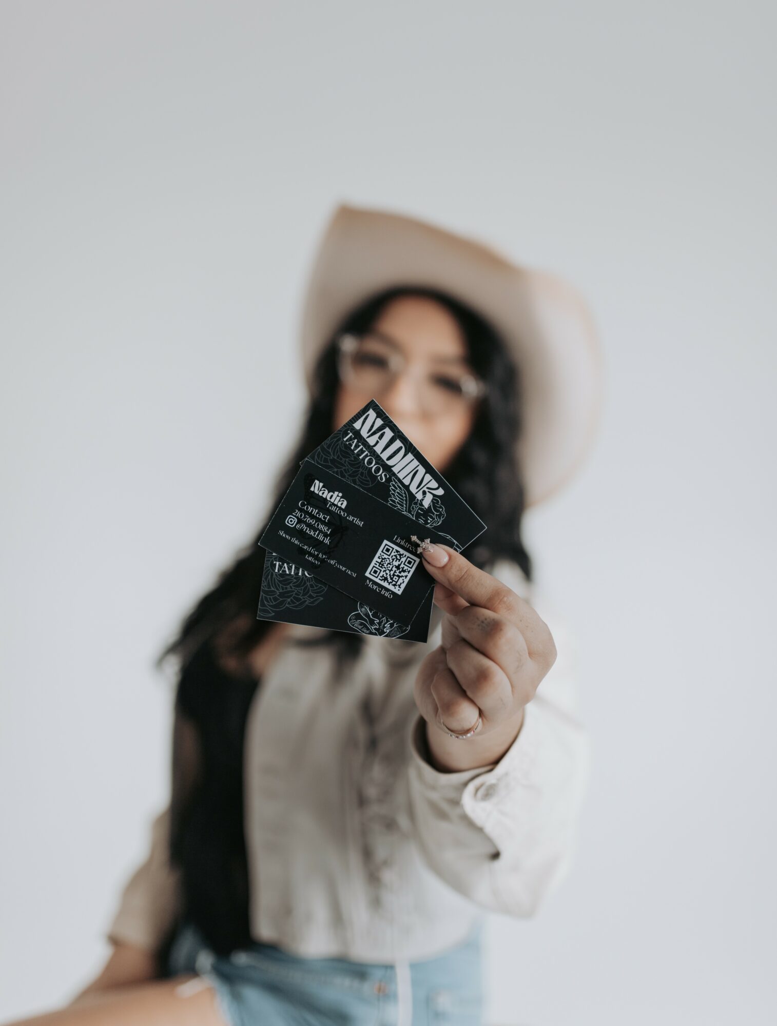 Person wearing a hat holding a ticket or card towards the camera, face slightly blurred, plain background.