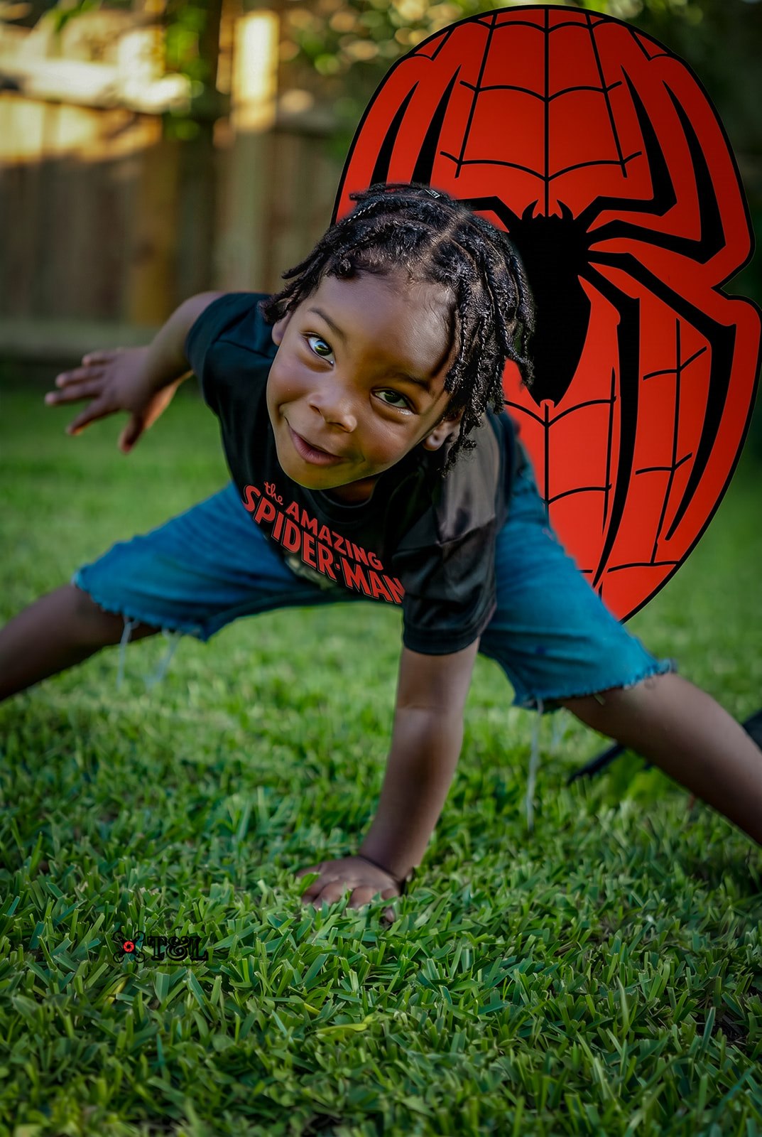 Child in a crawling position on grass, with a large Spider-Man logo in the background.