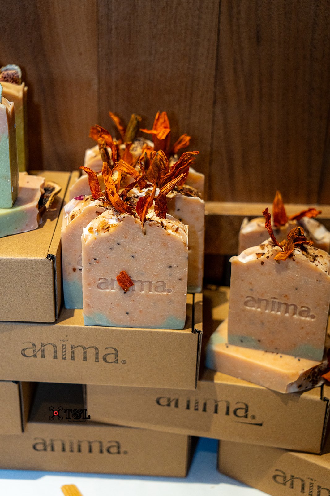 Two square-shaped soap bars with dried flower decorations on top, placed on boxes labeled 'anima.'