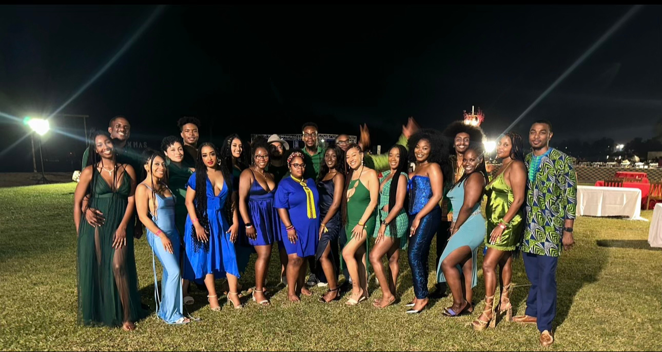 Group of people standing outdoors at night, dressed in formal attire, smiling for a photo on grass.