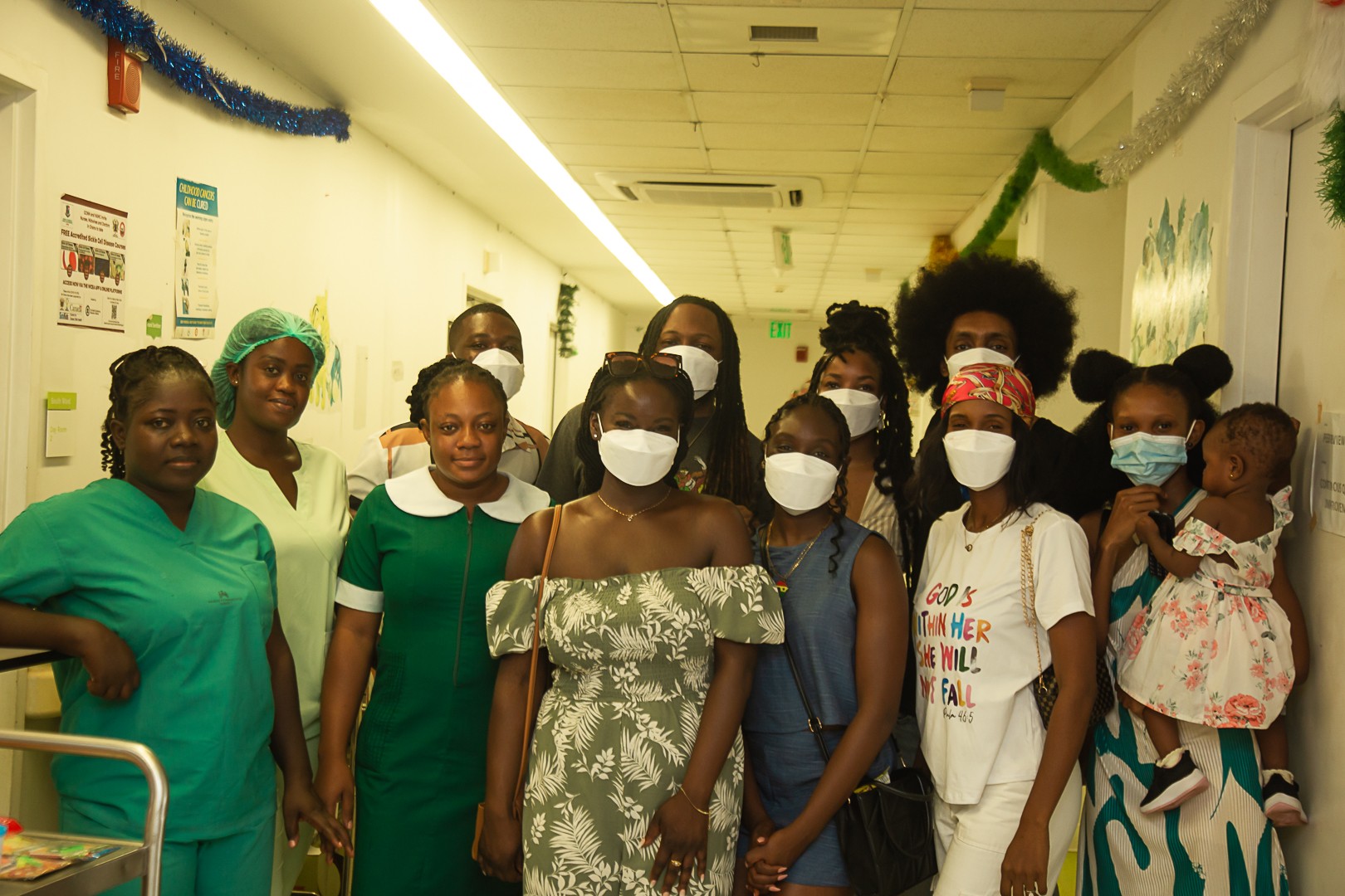 Group of people, some wearing masks, standing in a hallway decorated with green and blue streamers, some smiling.