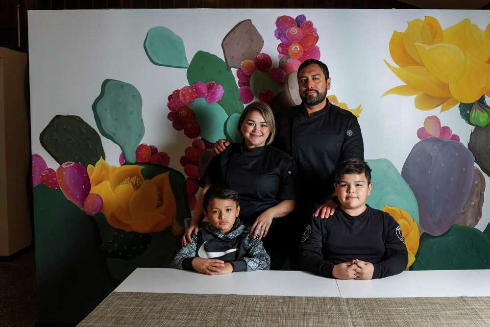 Family of four sitting in front of a colorful floral mural, with two children in front and two adults behind them.