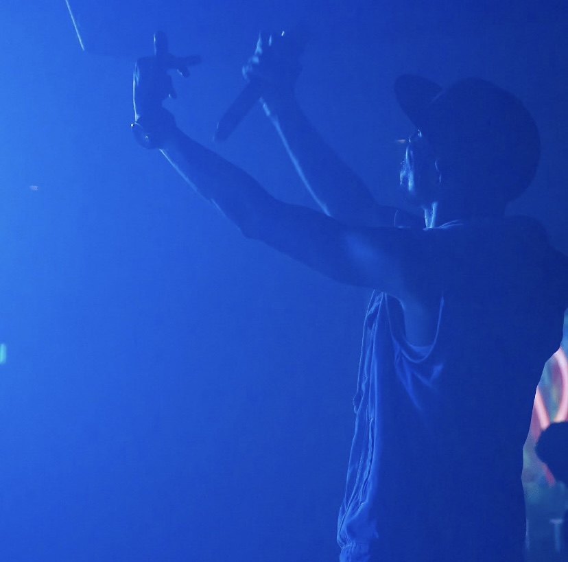Person wearing a hat, holding an object, in a blue-lit environment, facing right, with a blurred background.