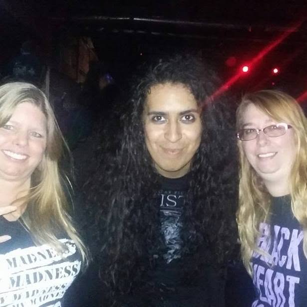 Three women smiling in a dark setting with red lights, two with blonde hair and one with dark curly hair.