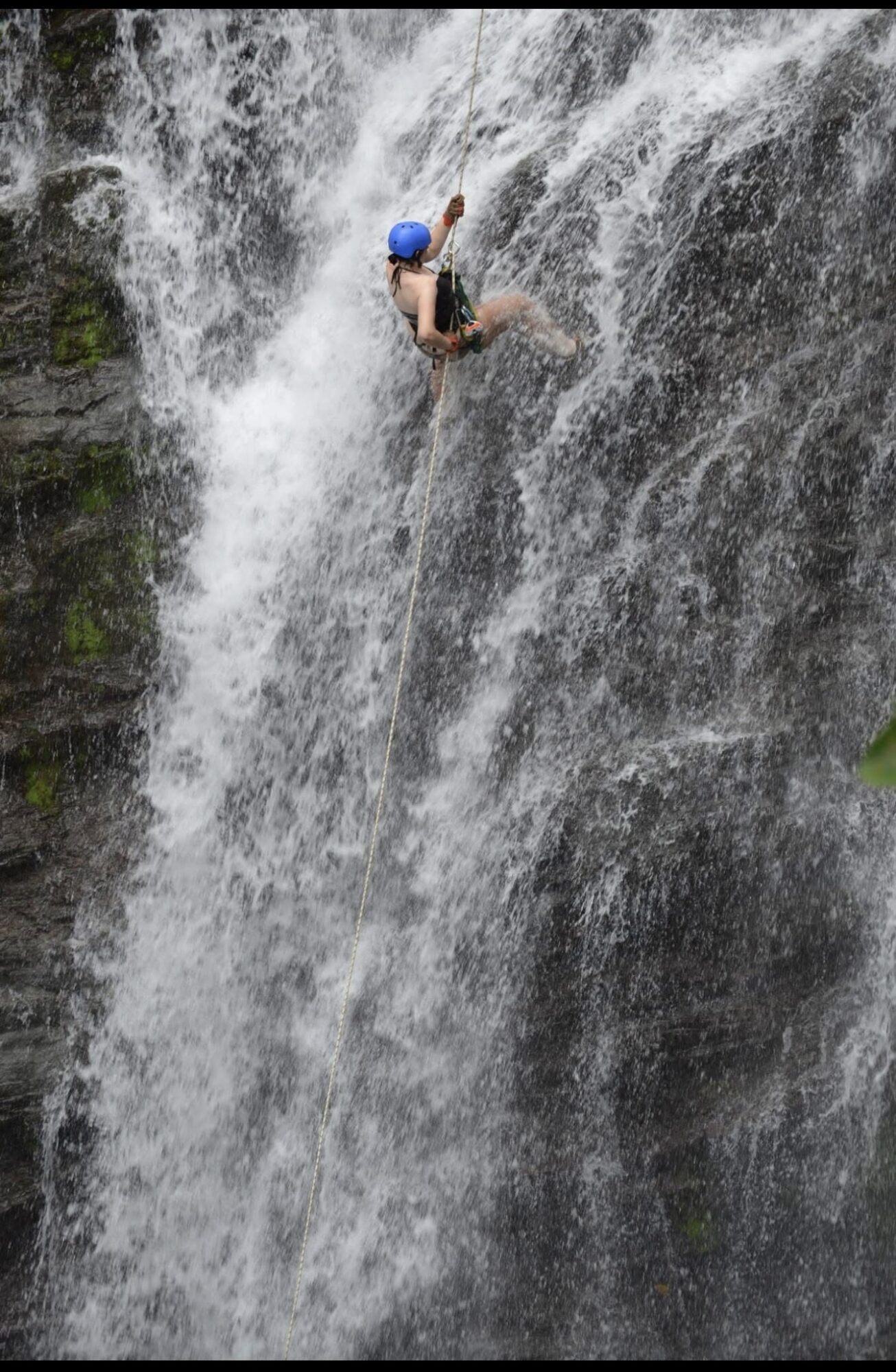 Person wearing a helmet climbing a waterfall with water cascading down the rocks.