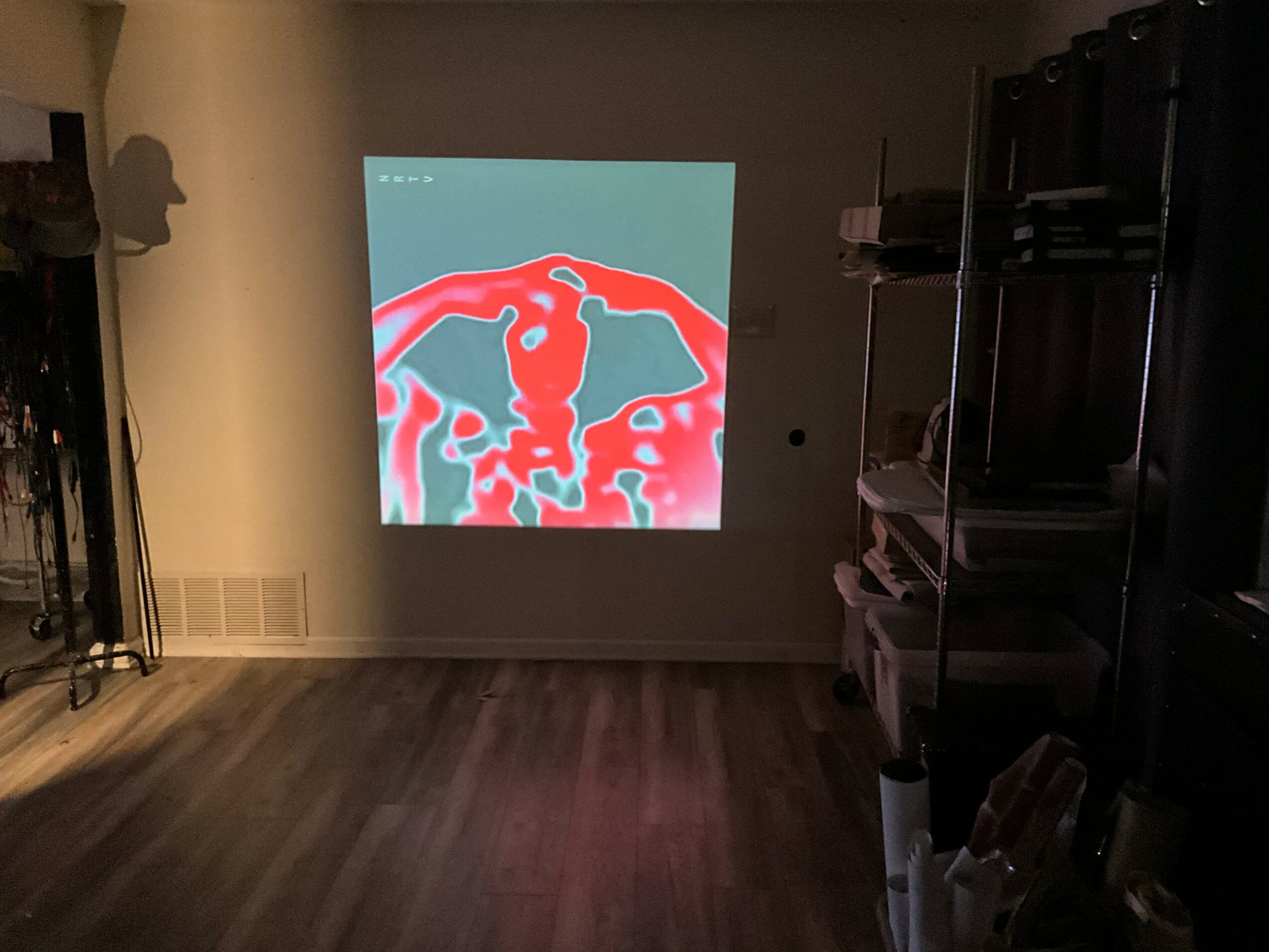 Projection on wall showing a red and blue abstract image, with a dark room and shelves on the right side.