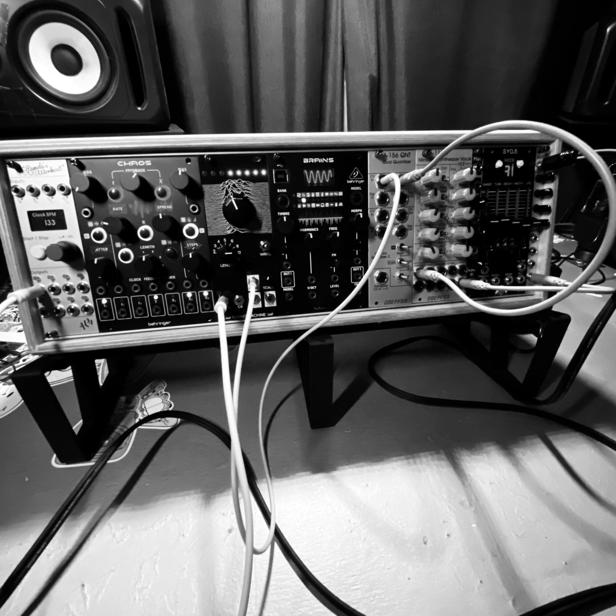 Electronic music synthesizer and modular synthesizer setup on a stand with cables connected, in a room with speakers and curtains