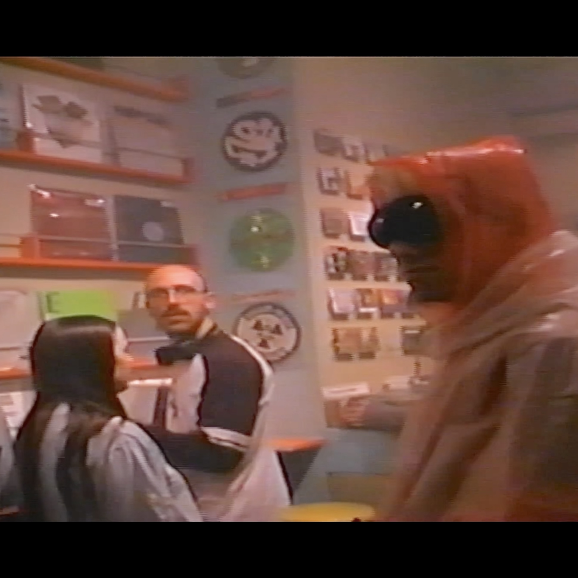 People in a store with shelves and posters, one person wearing a lion mask, two others facing away.
