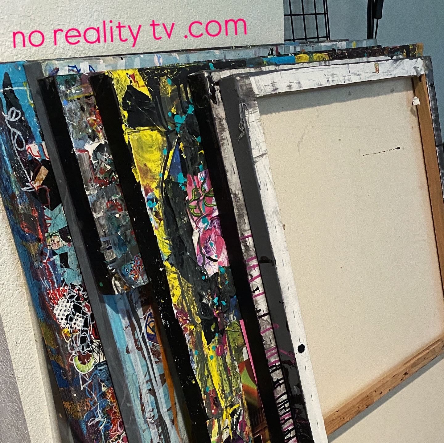 Multiple colorful, painted frames leaning against a wall, with a partially visible sign reading 'no reality tv.com' at the top.