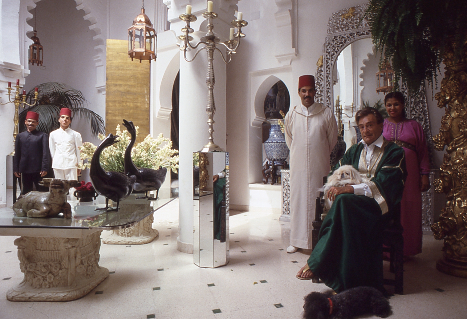 People in traditional attire inside a decorated room with ornate furniture and decor, including a black swan sculpture.