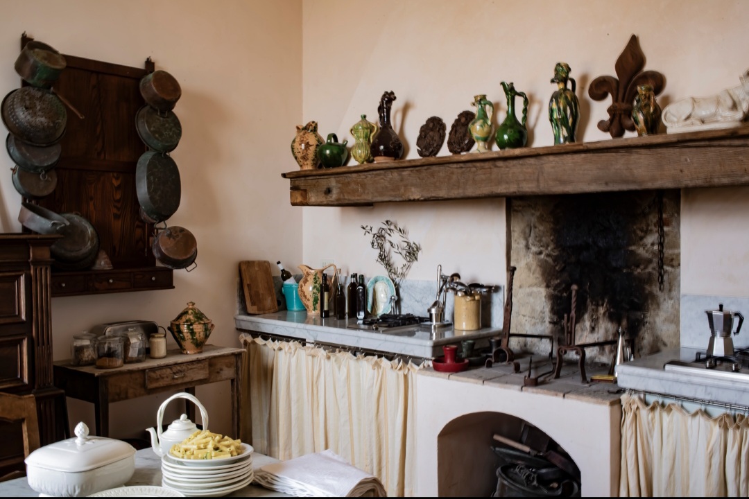 Kitchen with a wooden shelf holding decorative items, a stove, and a countertop with dishes and utensils, in a cozy room.