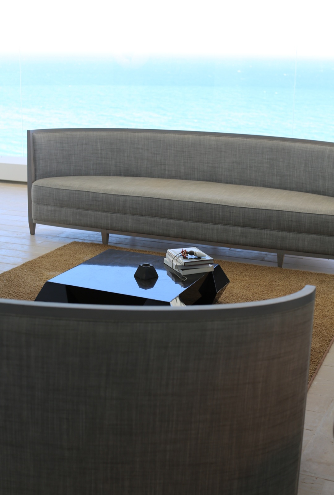 Living room with a gray sofa, a black coffee table, and a view of the ocean through large windows.