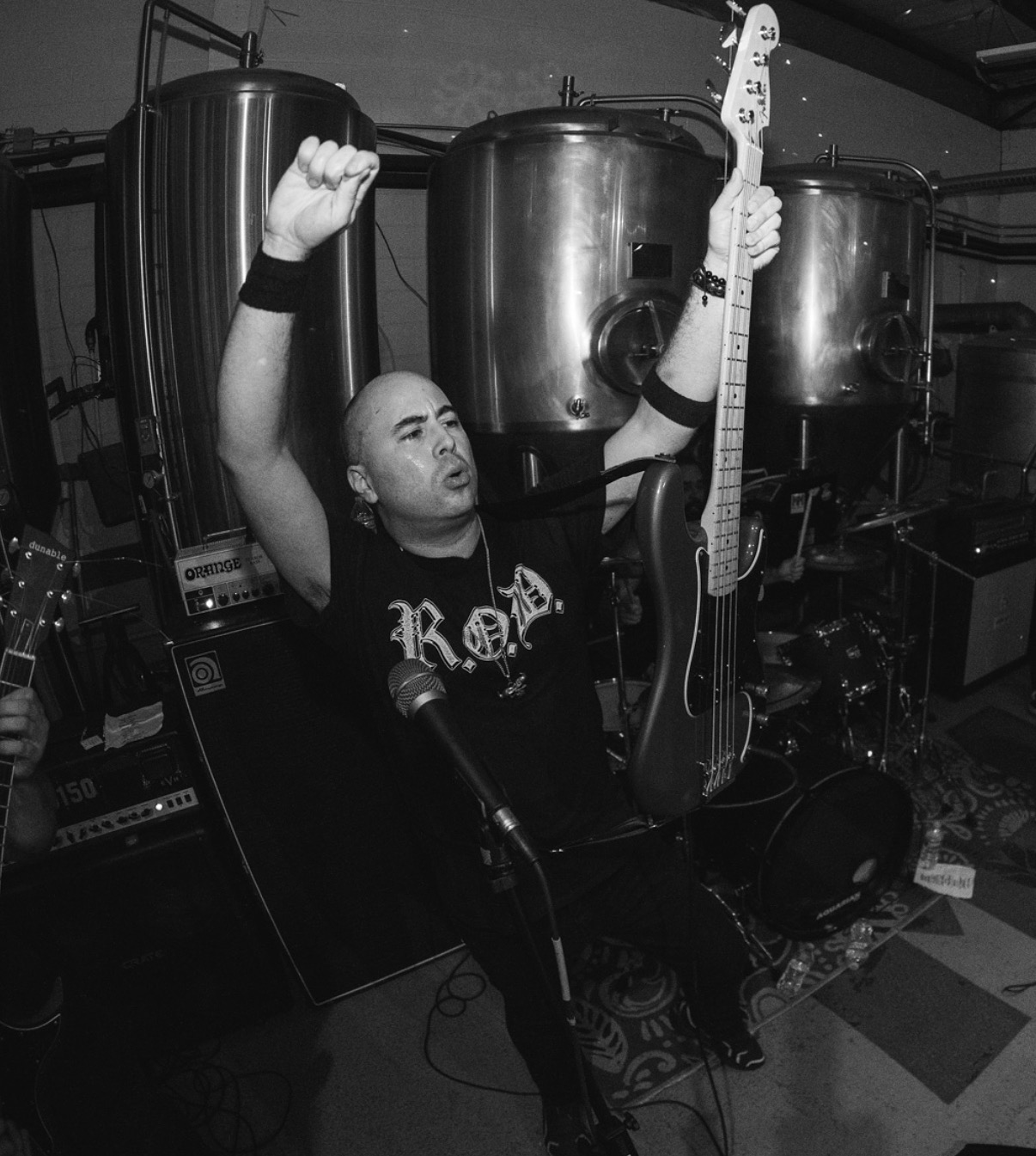 Person with raised fist holding a guitar, standing in a room with large metal tanks, microphone, and equipment.