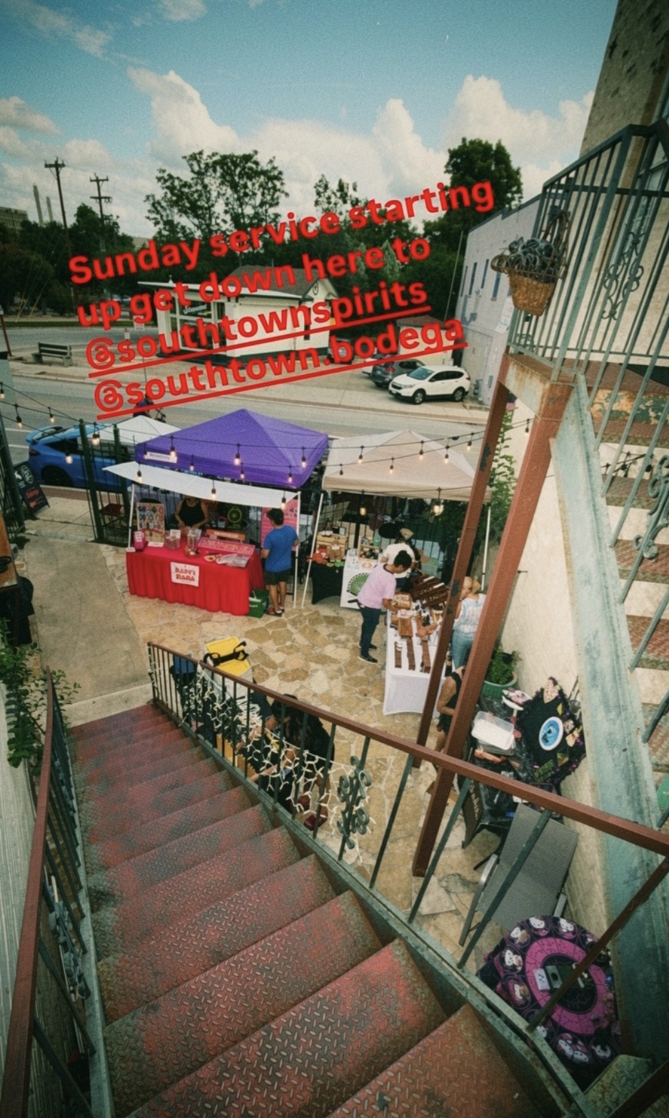 Staircase leading down to an outdoor event with tents and people, sky with clouds in background, text overlay in red.