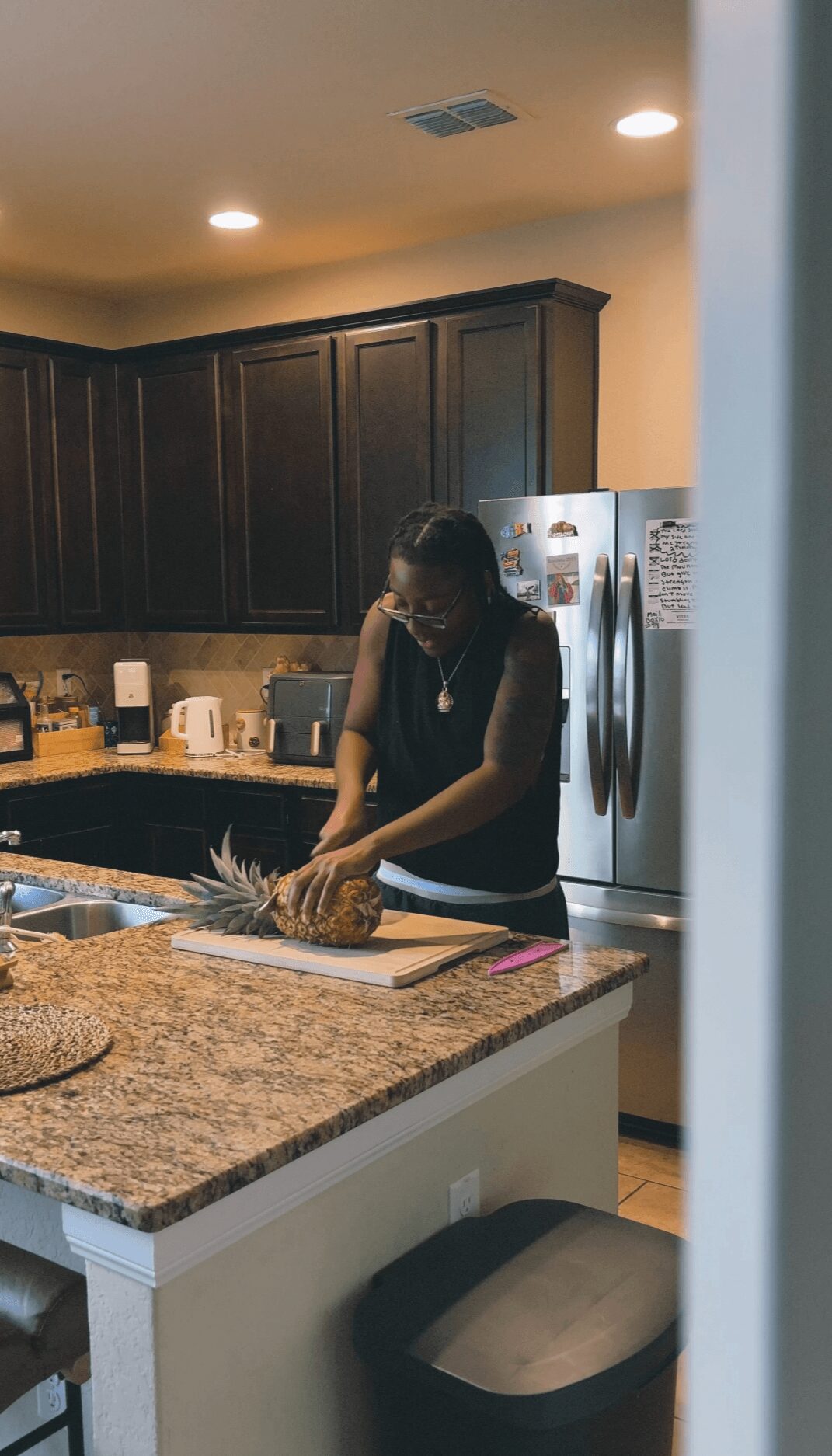 Woman preparing food on kitchen counter with dark cabinets and stainless steel refrigerator in background.