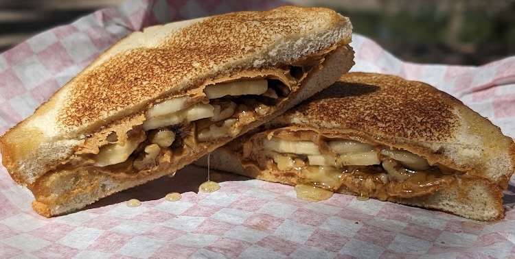 Sandwich with toasted bread and filling of sliced apples and caramelized onions, cut in half, on pink checkered paper