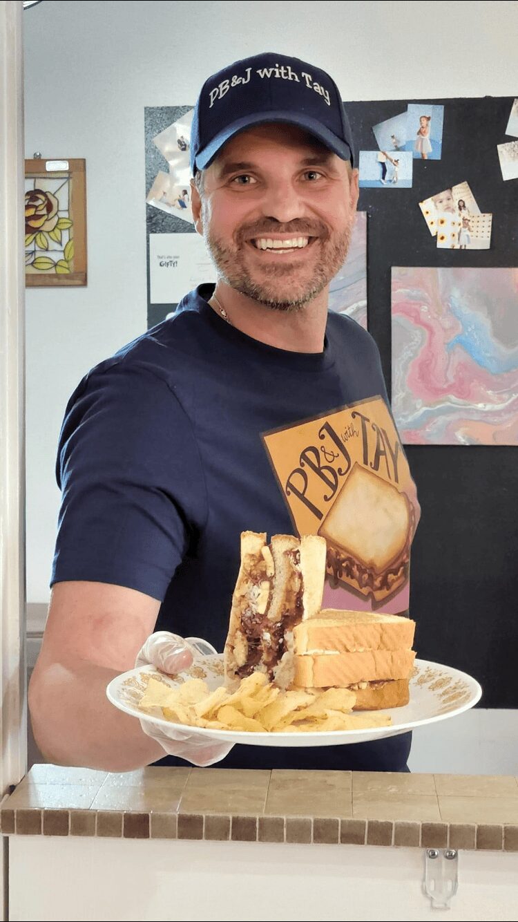 Smiling man holding a plate with cake slices and chips, wearing a cap and navy shirt, in a room with artwork