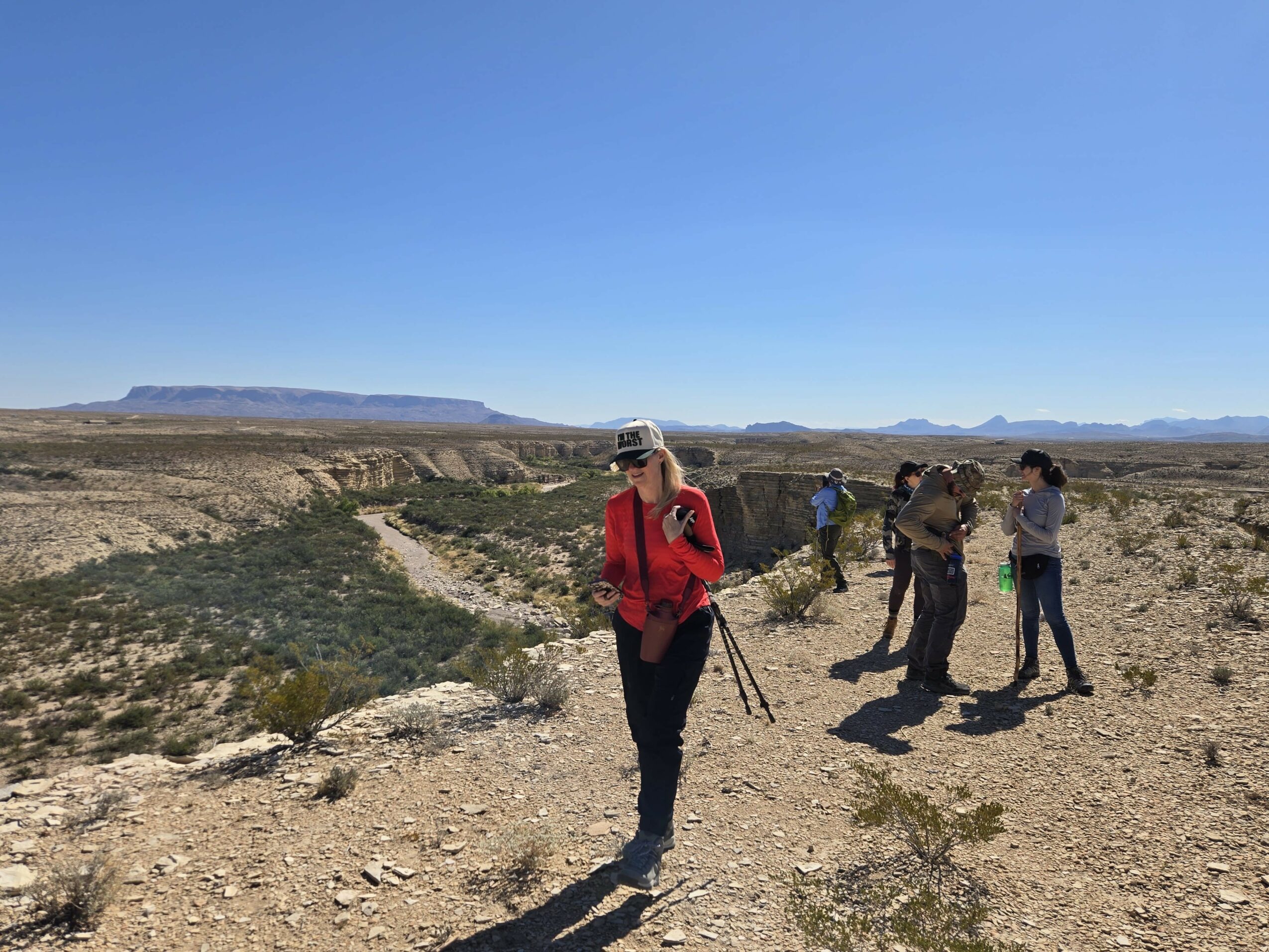 Group of people standing on a rocky desert landscape under a clear blue sky, with distant mesas in the background.